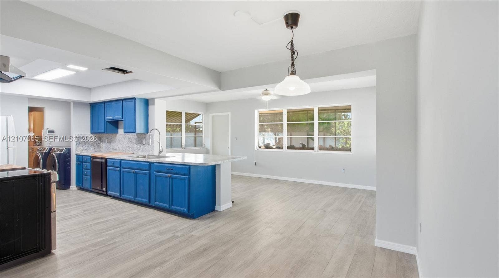 Kitchen featuring blue cabinetry, stone-finish countertops, a stainless steel sink with a goose-neck faucet, pendant lighting, and light-toned wood-finish flooring