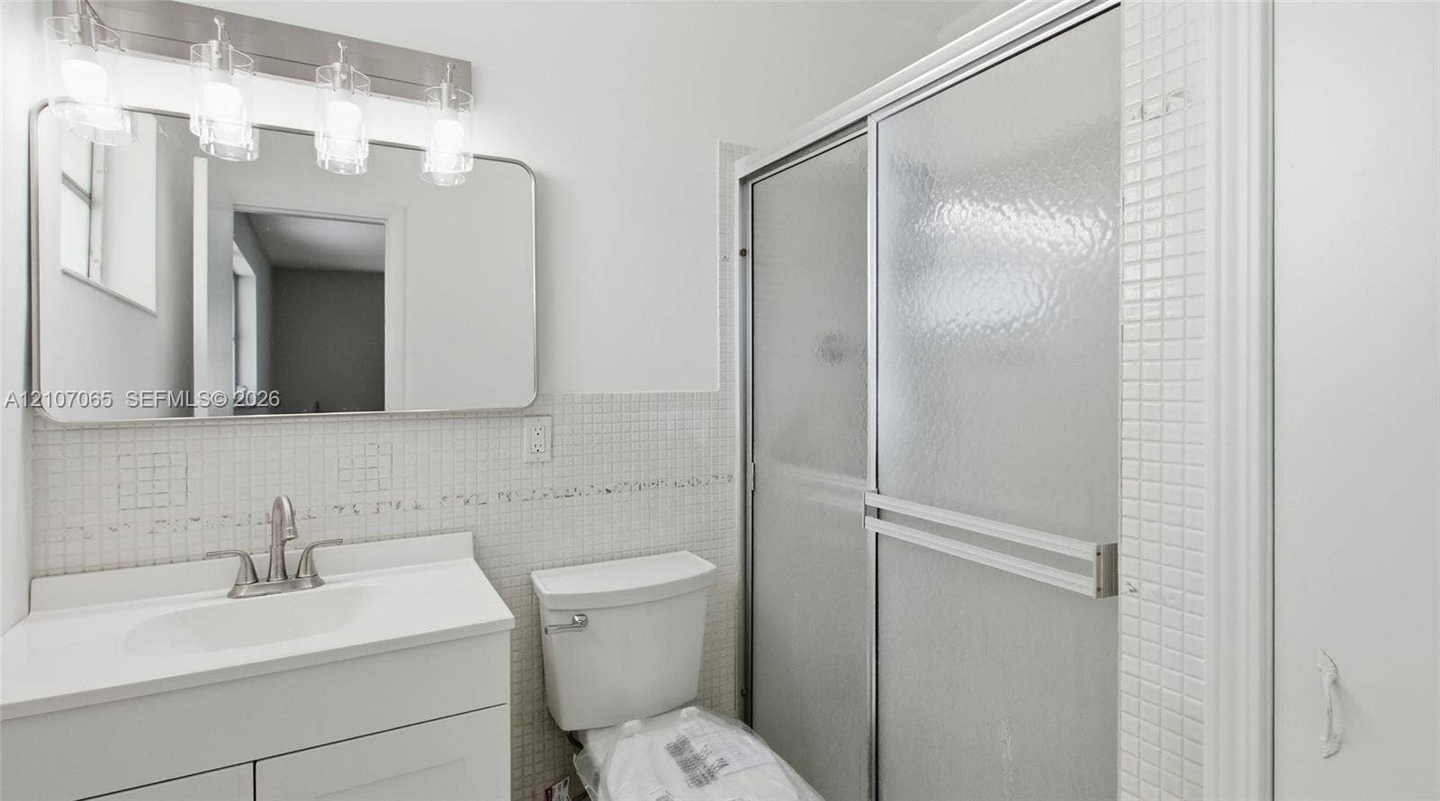 Bathroom featuring a white vanity cabinet, square wall-mounted mirror, four-light vanity fixture, and a shower enclosure with sliding glass doors