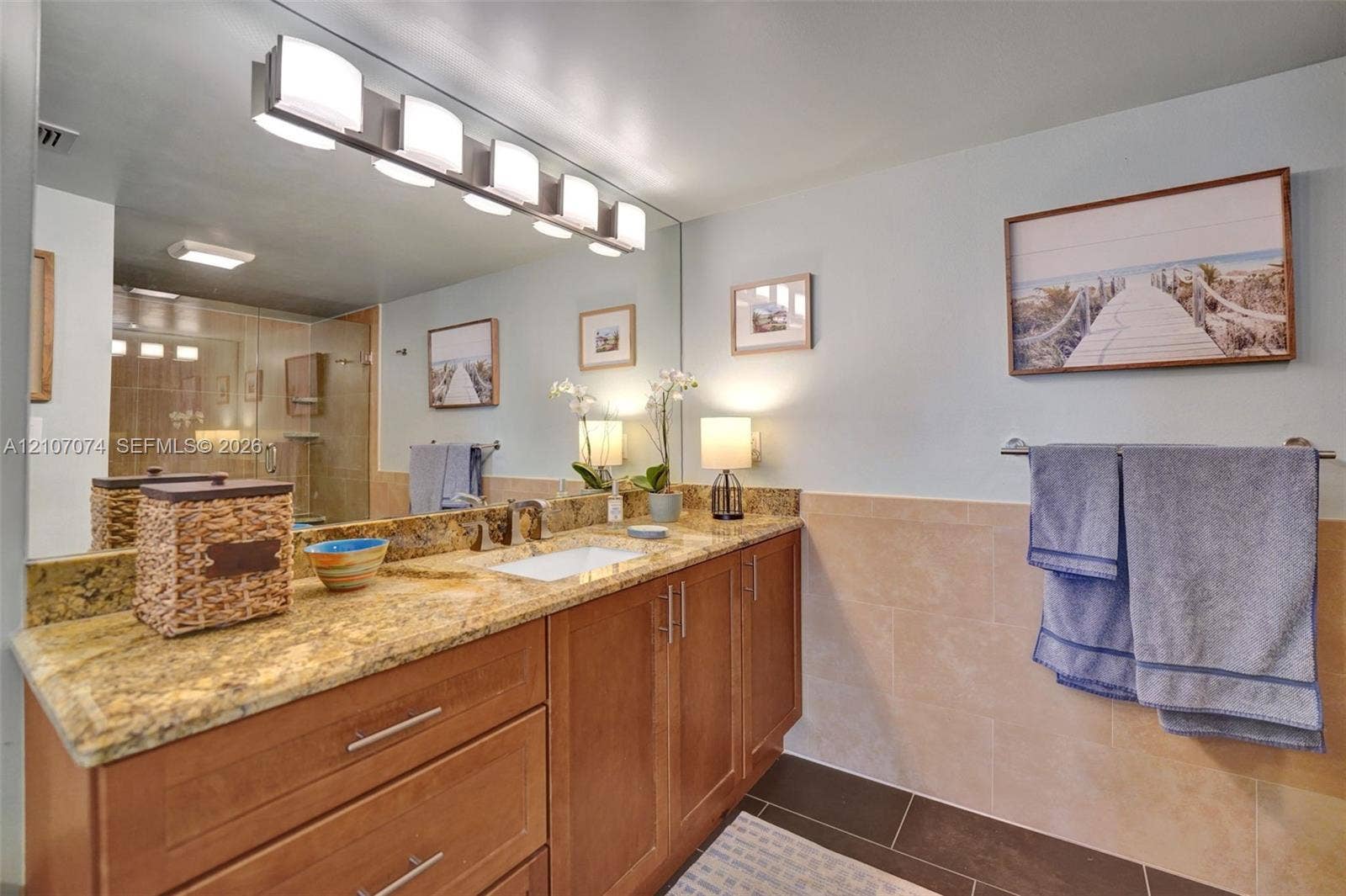 1201 S Ocean Drive, #218N, Hollywood, Hollywood, FL 33019 Natural stone countertop featuring an integrated rectangular undermount sink, cherry-tone wood cabinetry with brushed nickel hardware, full-width wall mirror, five-light overhead fixture, and tiled wall wainscoting
