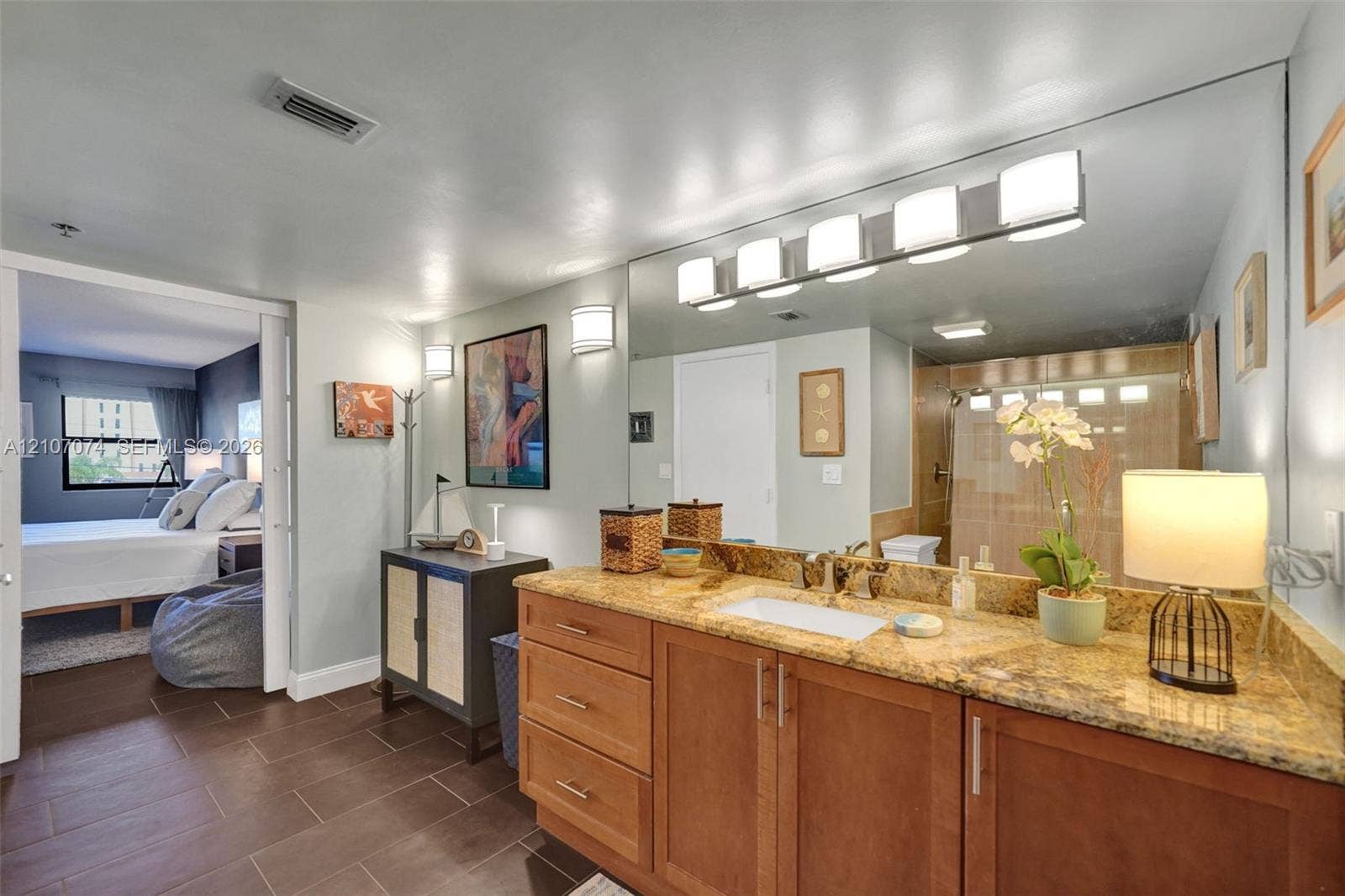 1201 S Ocean Drive, #218N, Hollywood, Hollywood, FL 33019 Bathroom vanity with natural stone countertop, integrated rectangular sink, wooden cabinetry, and expansive wall-mounted mirror featuring integrated light fixtures