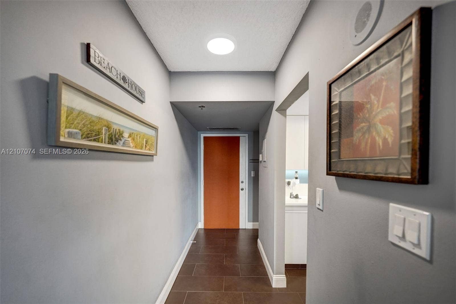 1201 S Ocean Drive, #218N, Hollywood, Hollywood, FL 33019 Hallway featuring large-format ceramic tile flooring, neutral grey wall paint, and a bold orange solid-core entry door