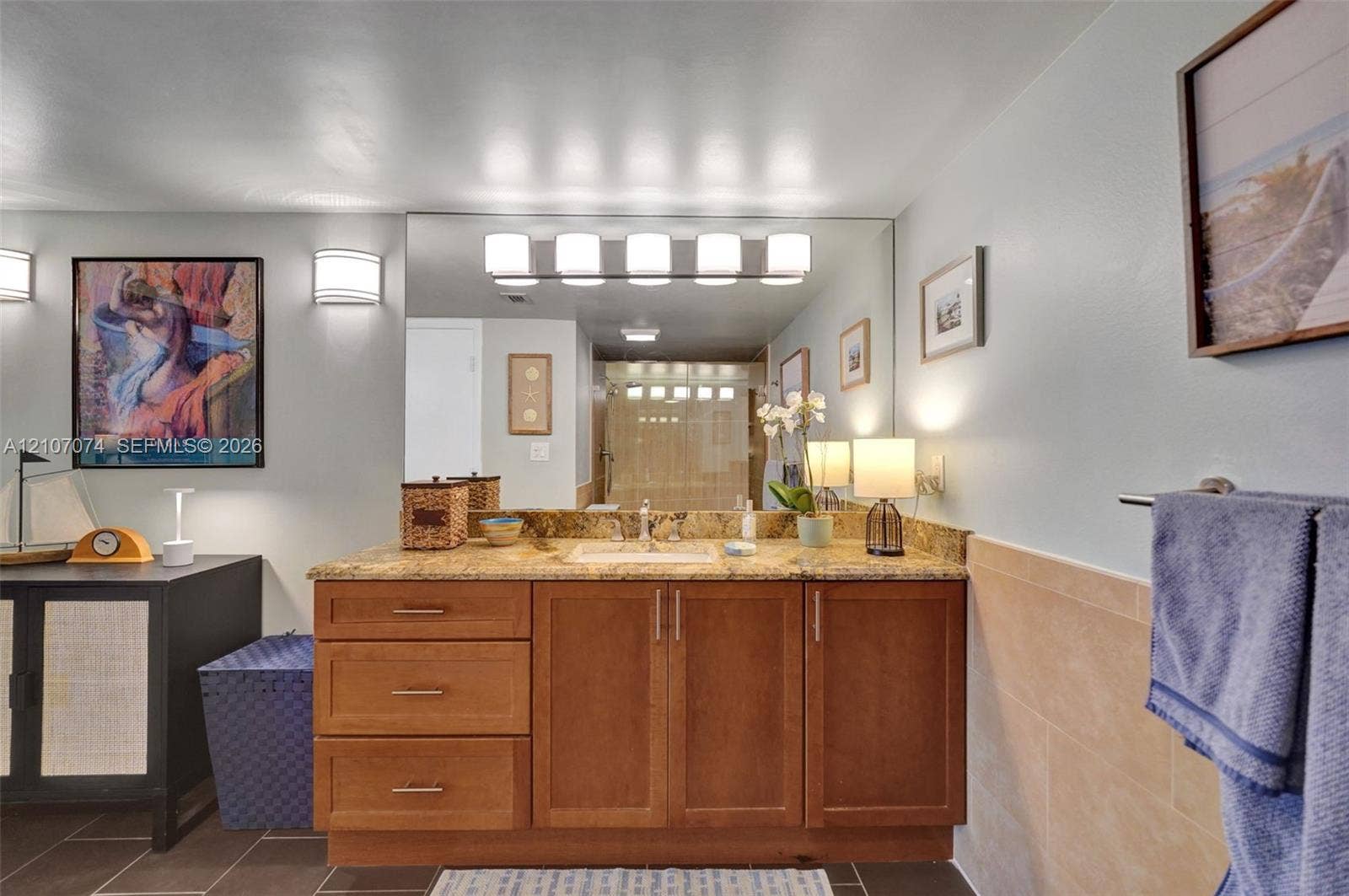 1201 S Ocean Drive, #218N, Hollywood, Hollywood, FL 33019 Wood-finish vanity cabinetry with an integrated countertop, large wall-mounted vanity mirror, five-light fixture, and ceramic tile wainscoting