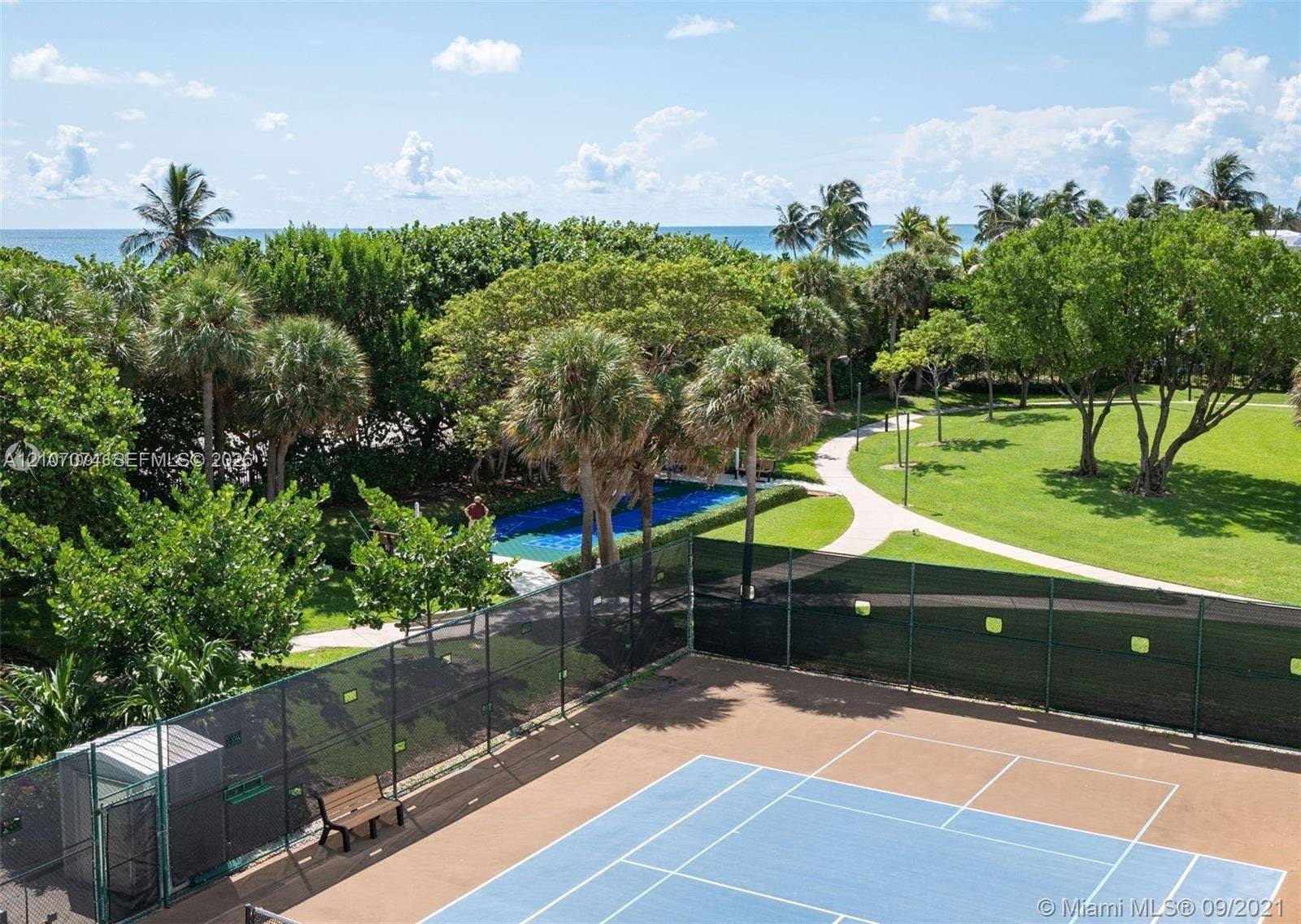 1201 S Ocean Drive, #218N, Hollywood, Hollywood, FL 33019 Tennis court with fenced perimeter, paved walking paths, manicured lawns, mature palm trees, and ocean backdrop