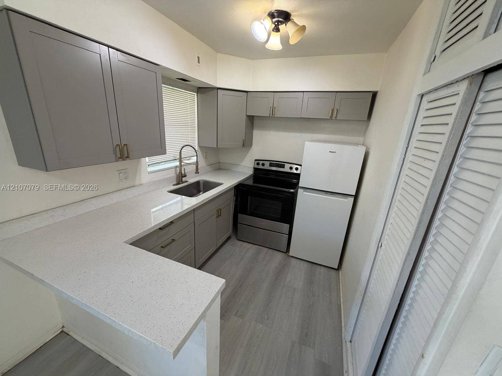 2450 Lincoln Street, #3, Hollywood, Hollywood, FL 33020 Kitchen featuring gray shaker-style cabinetry, solid-surface countertops, wood-finish flooring, undermount stainless steel sink, and built-in closet with louvered doors