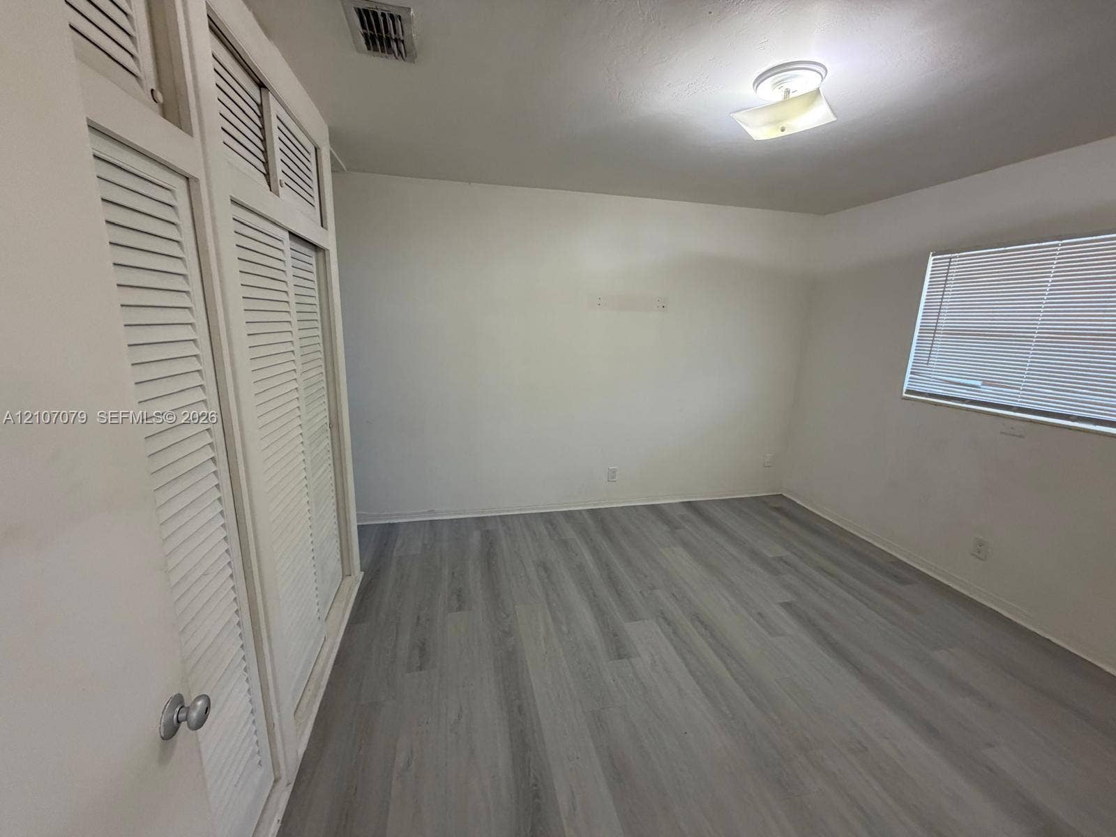 2450 Lincoln Street, #3, Hollywood, Hollywood, FL 33020 Room featuring wood-finish flooring, built-in louvered-door closets with overhead storage, a multi-pane window with horizontal blinds, and a centered flush-mount ceiling fixture