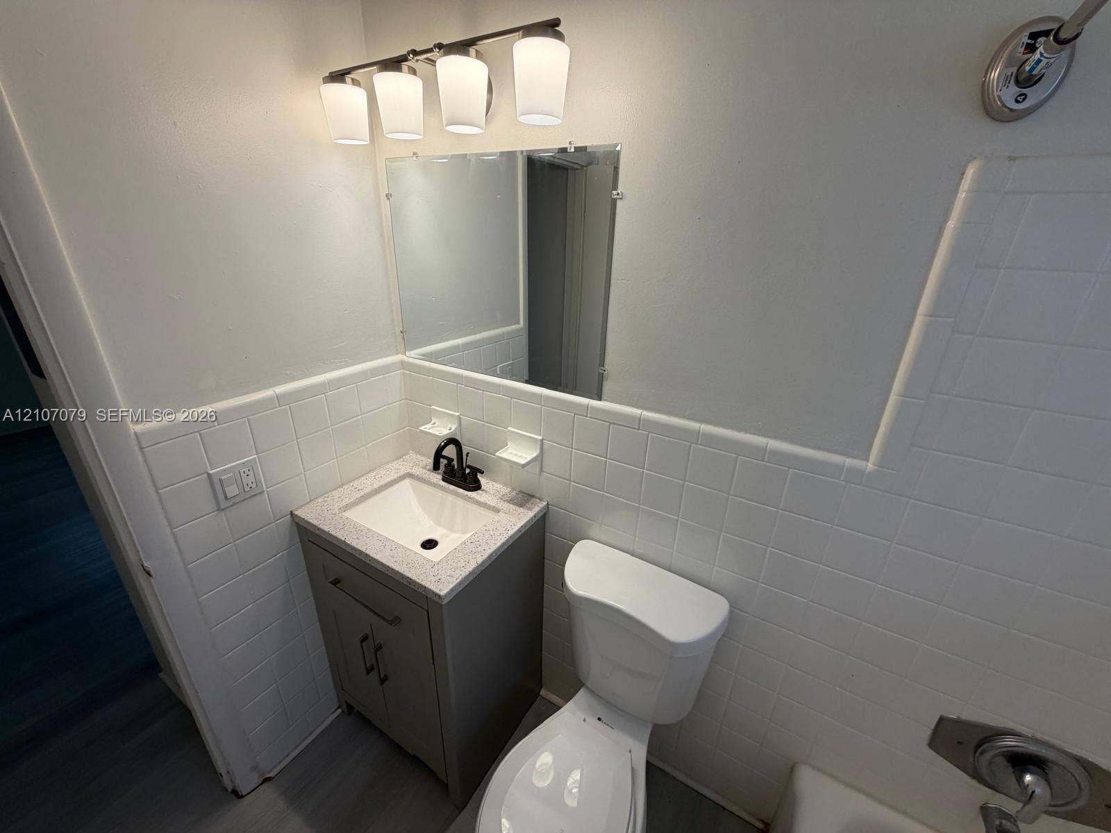 2450 Lincoln Street, #3, Hollywood, Hollywood, FL 33020 Bathroom featuring a vanity cabinet with a stone-composite countertop, undermount sink, matte black faucet, wall-mounted light fixture, and tile wall surfacing