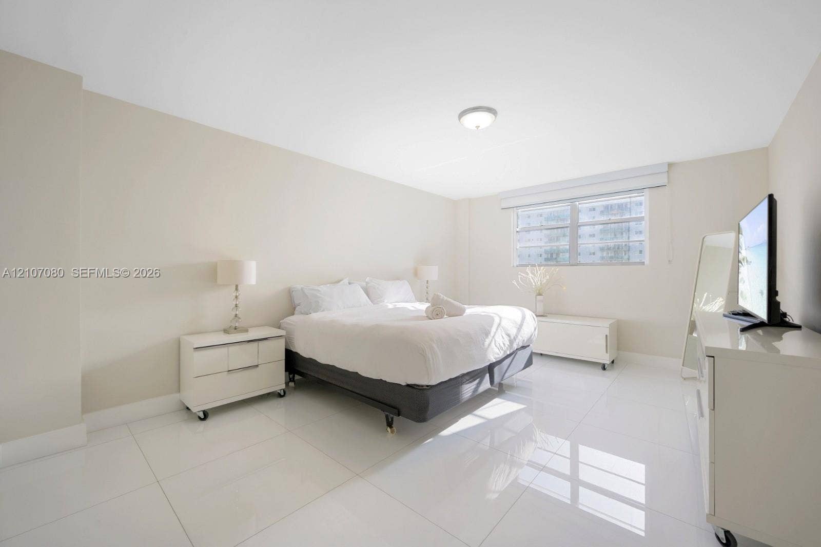 Spacious room featuring polished tile flooring, neutral wall tones, flush-mount ceiling lighting, and a large window with fitted blinds