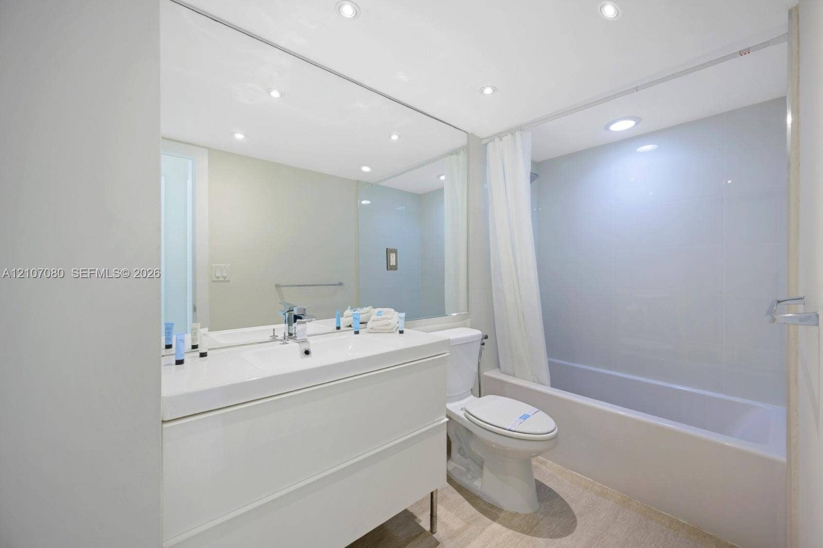 Modern white vanity with a rectangular sink, expansive wall-to-wall mirror, recessed ceiling lighting, and a full-height tile surround in the shower-tub combination