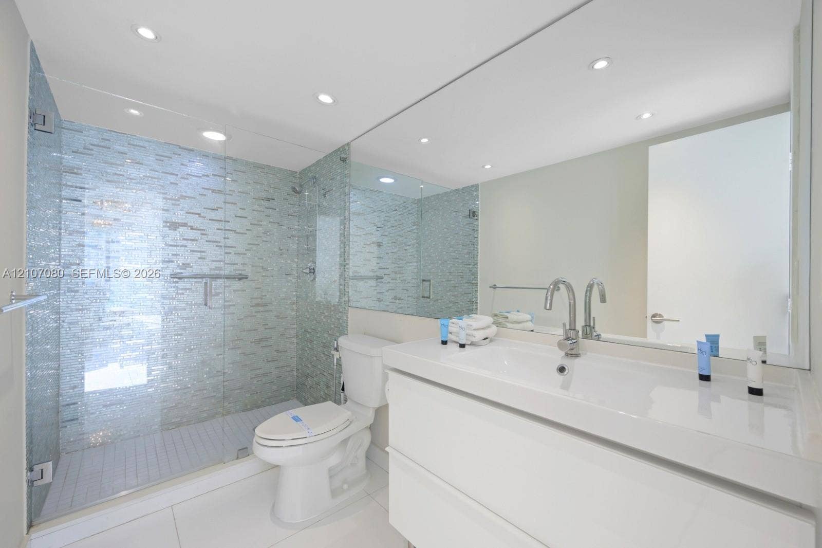 Walk-in shower with glass enclosure and mosaic tile surround, white floating vanity with integrated basin, polished chrome faucet, and expansive wall-to-wall mirror