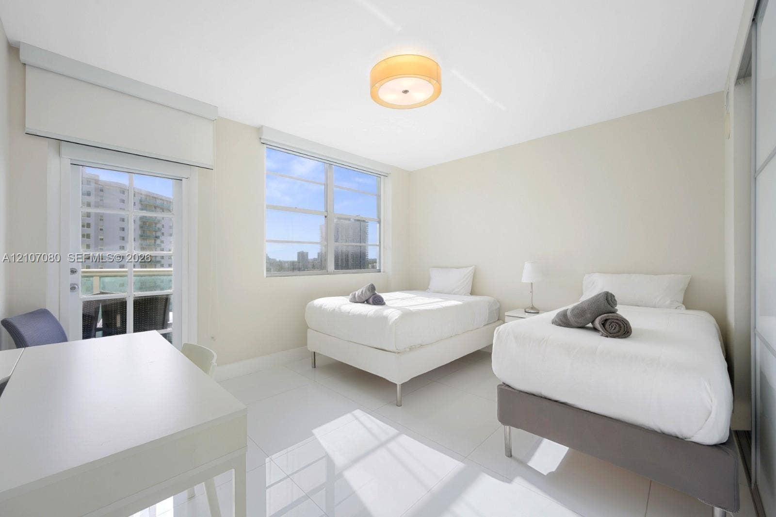 Bright room featuring polished white tile flooring, neutral wall tones, a central drum-style ceiling light fixture, large windows, and a glass-paneled door with an integrated exterior balcony
