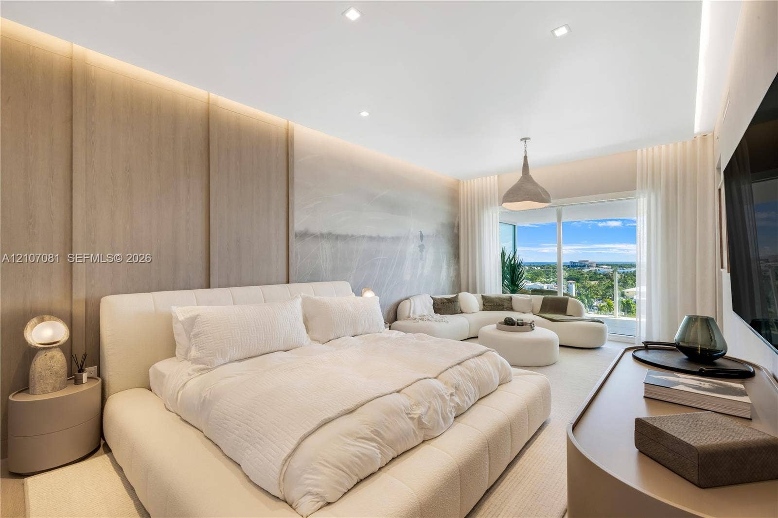 Wood-finish paneled accent wall, recessed lighting, integrated cove lighting, and floor-to-ceiling glass sliding doors opening to a balcony
