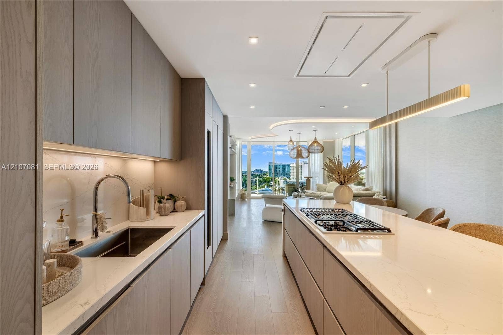 Contemporary kitchen featuring flat-panel cabinetry, light-toned stone countertops, a large center island with an integrated gas cooktop, wood-finish flooring, and recessed ceiling lighting