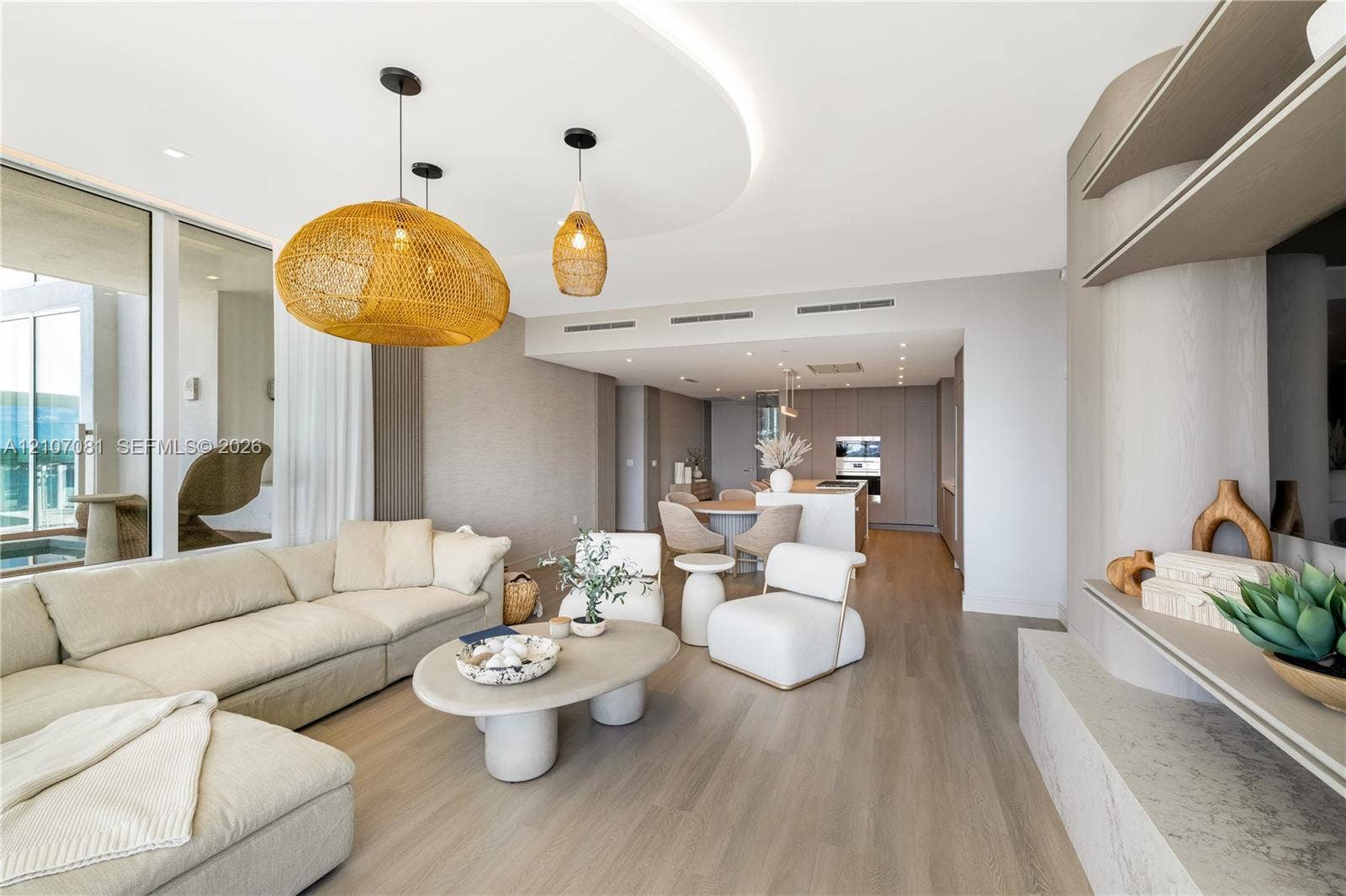 Open-concept living space featuring wood-finish flooring, recessed cove lighting, a custom built-in media console with stone-finish surfaces, and large-format sliding glass doors