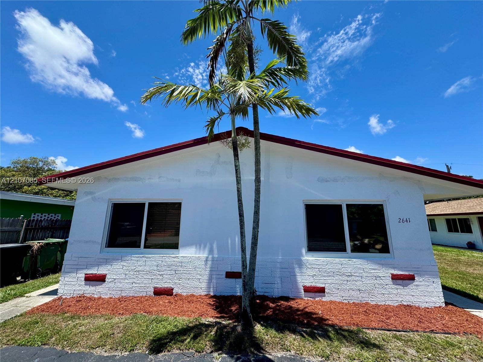 2641 SW 13th Avenue, #1, Fort Lauderdale, Fort Lauderdale, FL 33315 Exterior facade featuring a white stucco finish, painted brick wainscoting, sliding windows, and a prominent palm tree