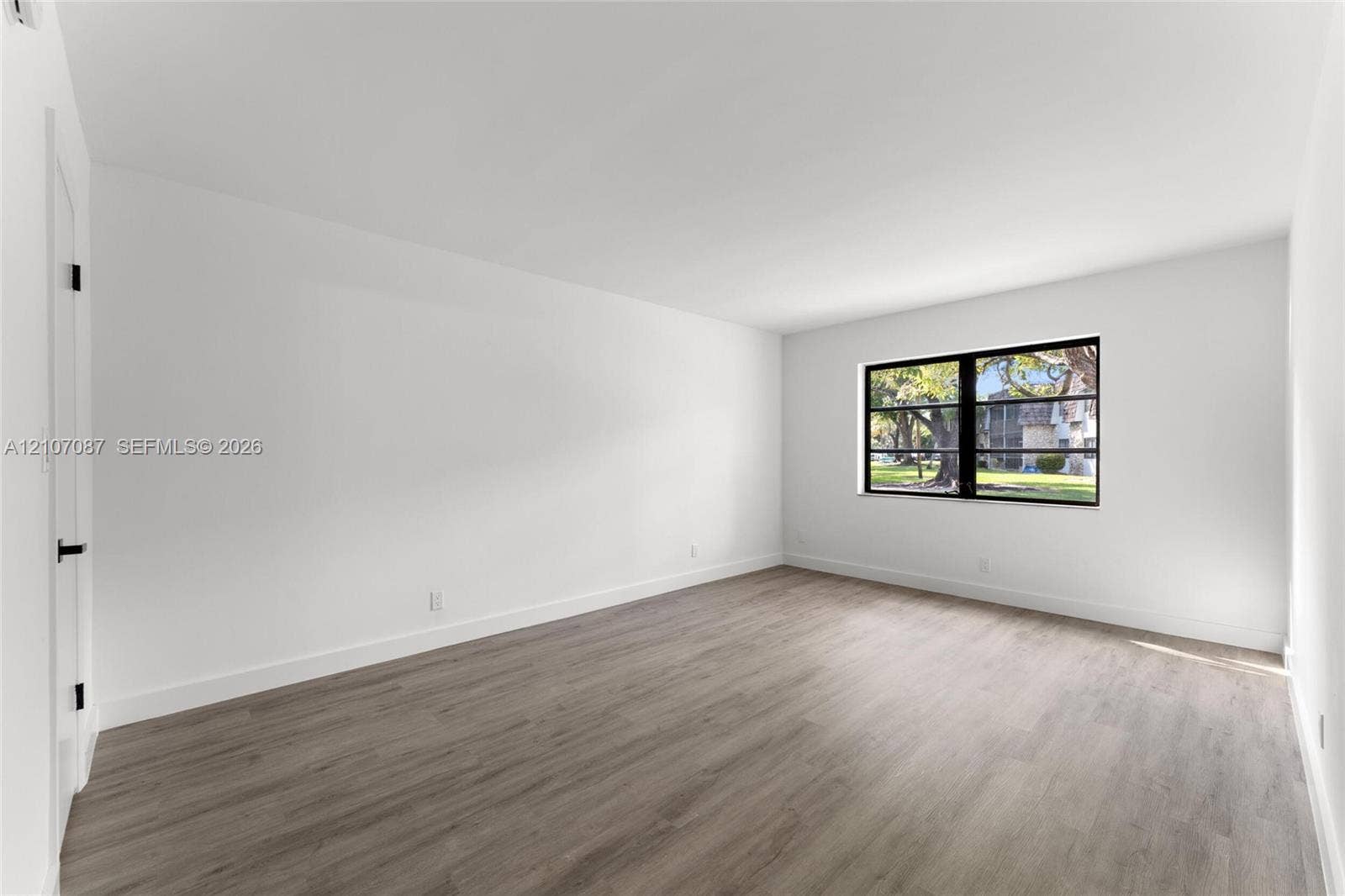Neutral-toned wood-finish flooring, crisp white walls, and a large window featuring a black frame