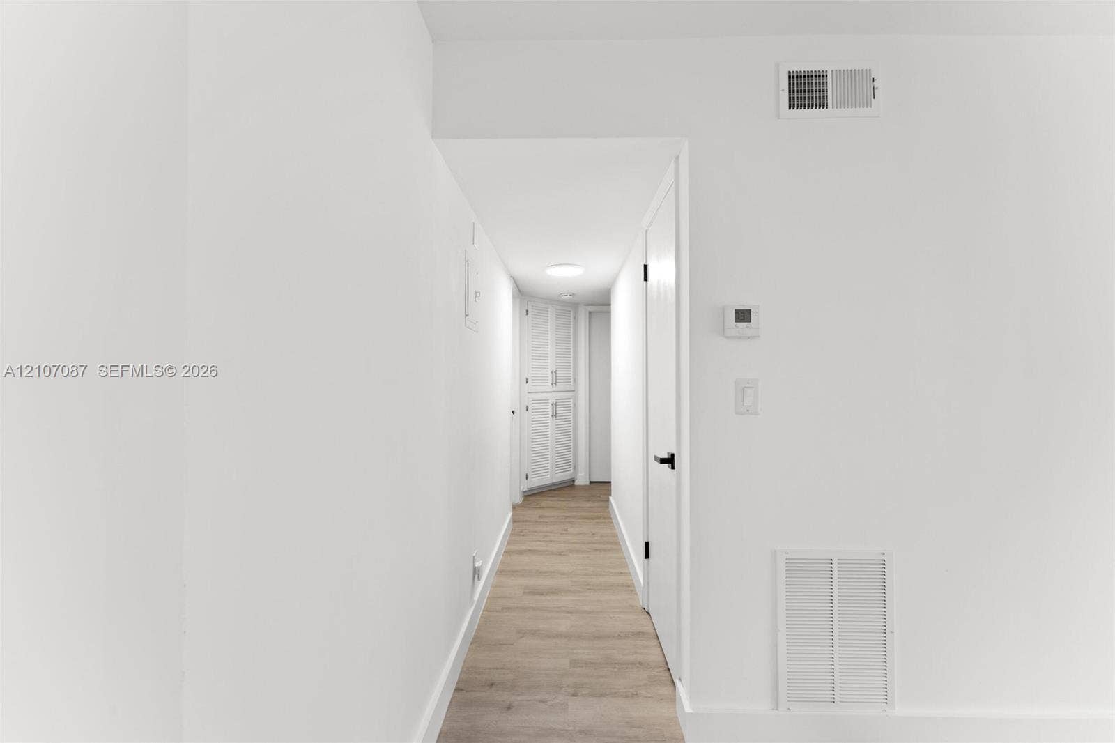 Hallway featuring wood-finish flooring, white walls, louvered built-in cabinetry, and matte black door hardware