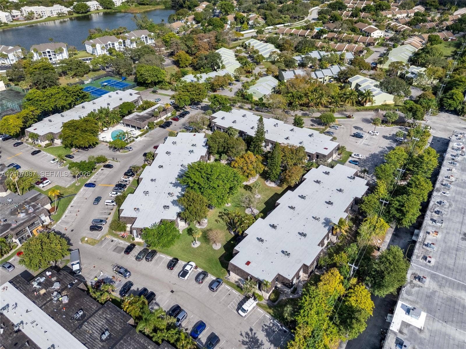 Aerial perspective of a multi-unit complex featuring mature trees, expansive green space, surface parking, and exterior lighting fixtures