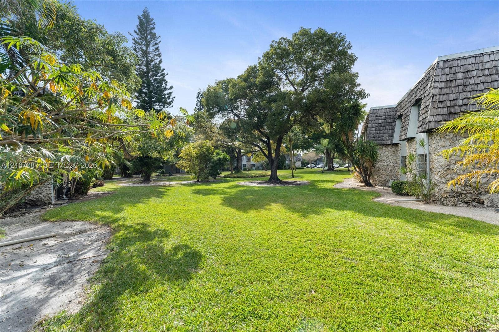 Expansive grounds featuring a manicured lawn, mature trees, stone exterior siding, and a mansard roof with shingle detailing