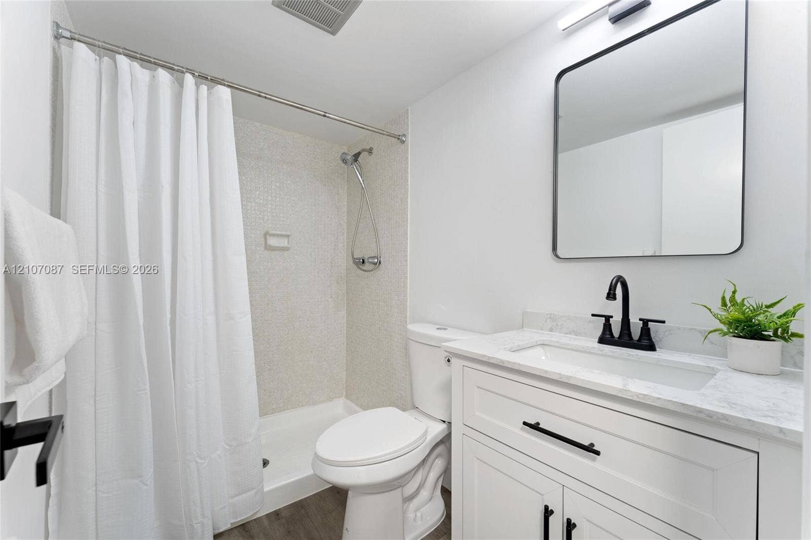 Bathroom featuring a white shaker-style vanity with stone-top surfacing, integrated rectangular sink, matte black hardware, and a shower with mosaic tile surround