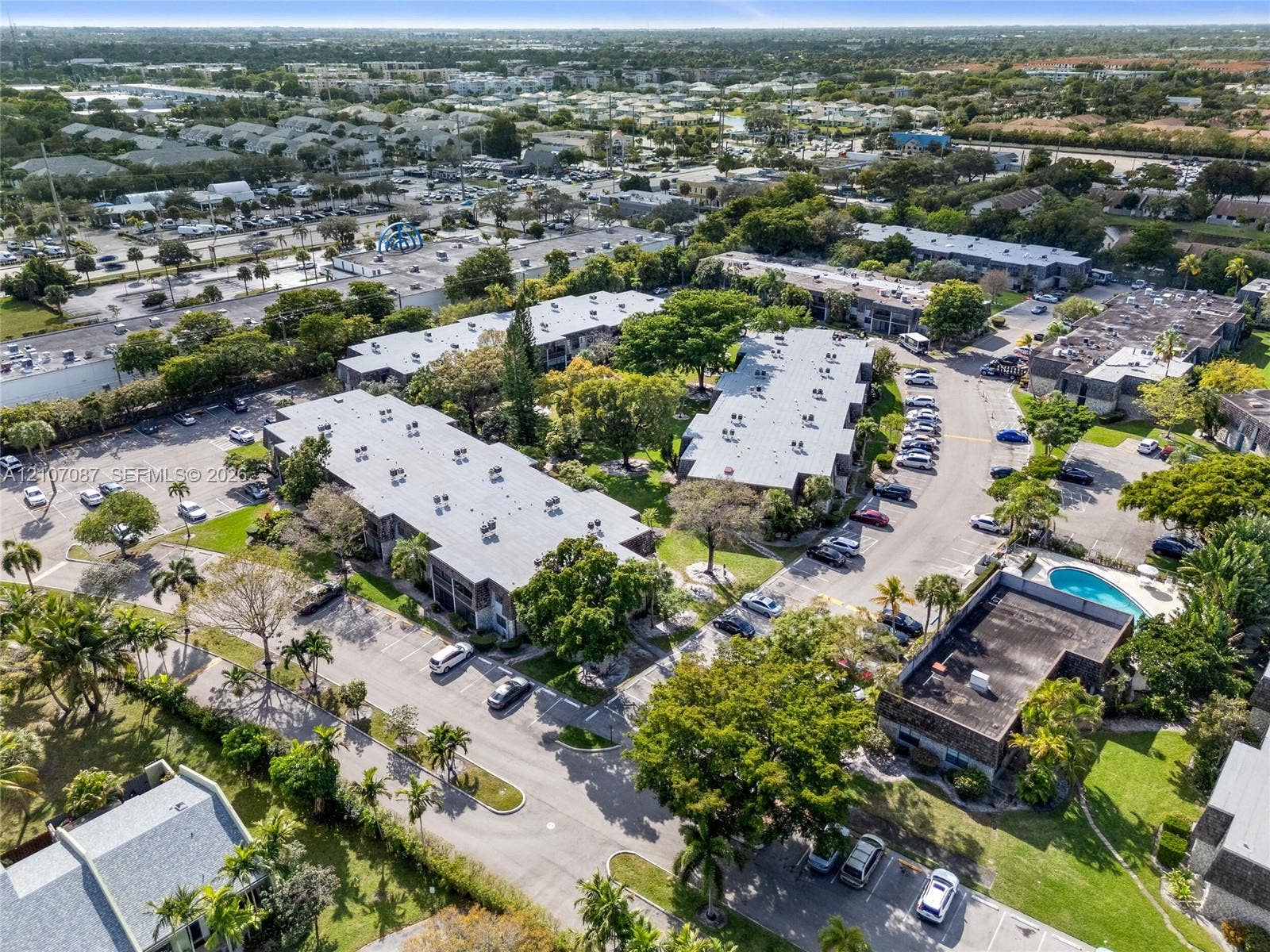 Multi-story residential complex featuring low-slope roofing, asphalt surface parking, mature landscaping, and an outdoor swimming pool