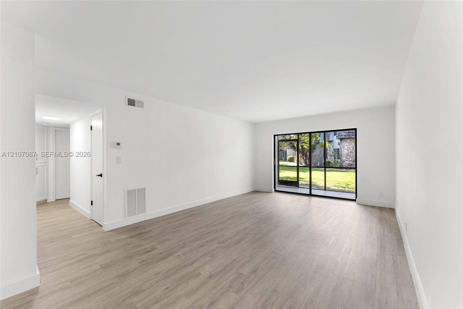 Neutral interior featuring wood-finish flooring, smooth white walls, and floor-to-ceiling sliding glass doors with black frames