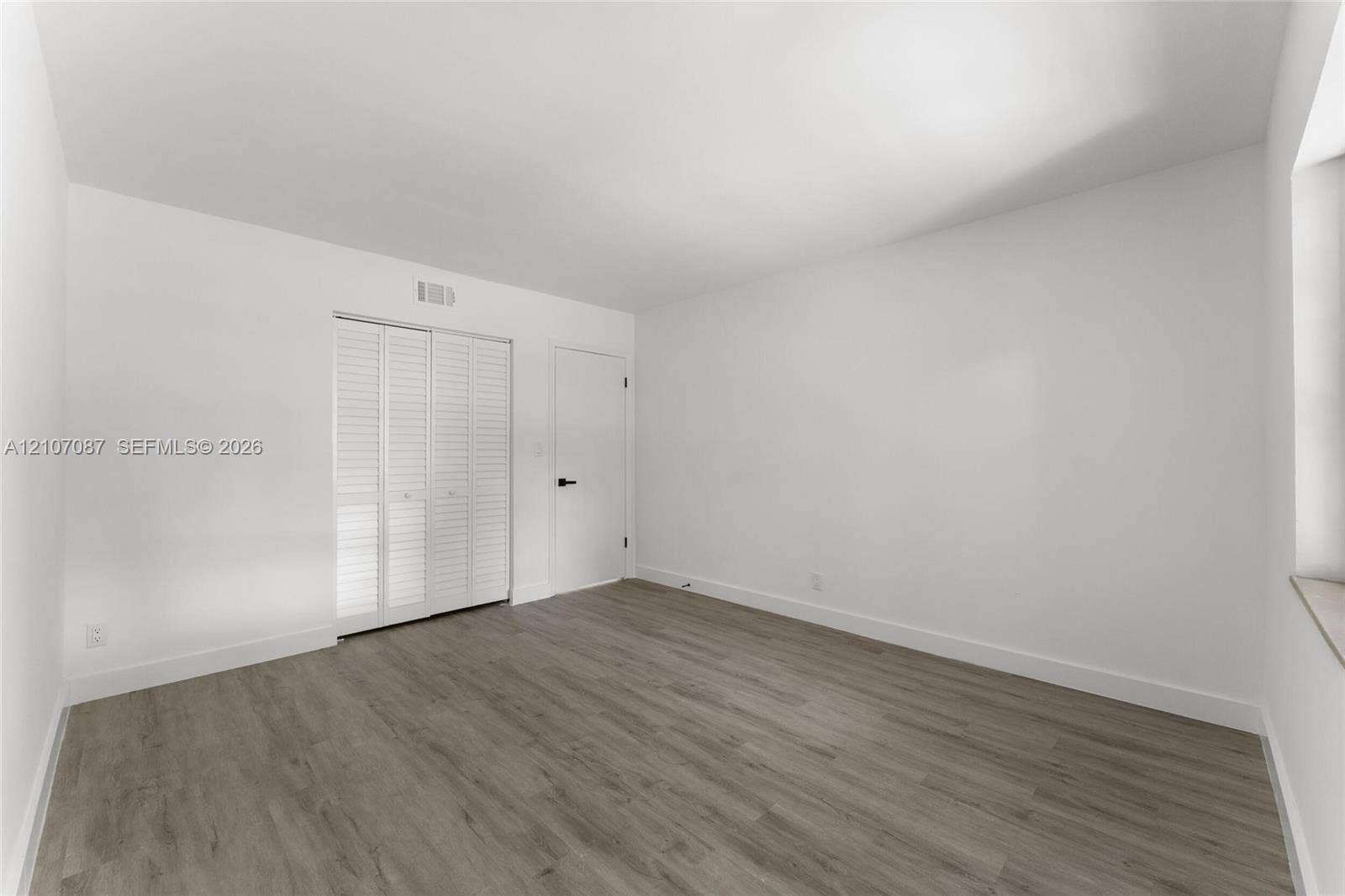 Room featuring wood-finish flooring, white walls, and a closet with white louvered bifold doors
