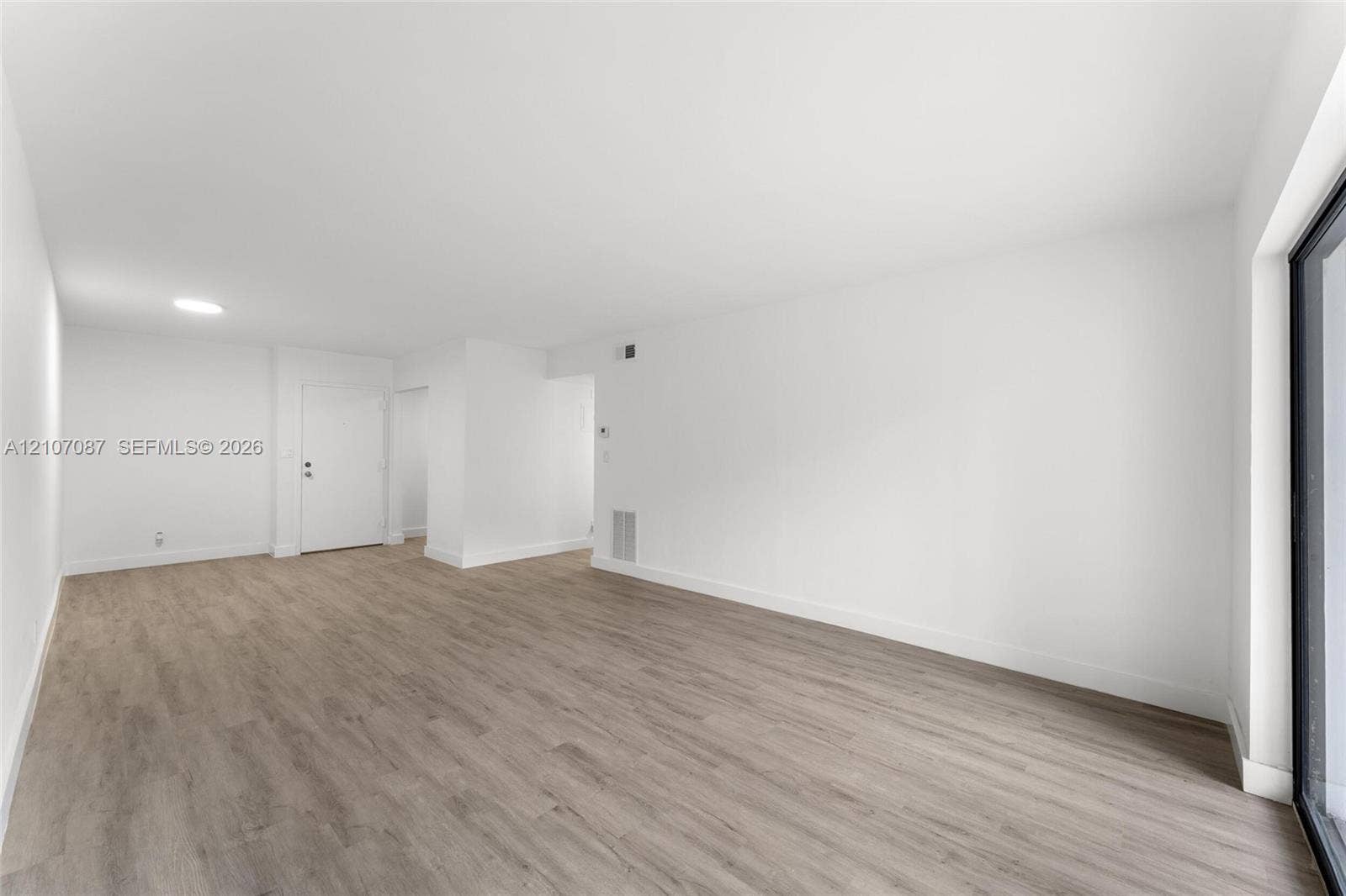 Open-concept interior space featuring neutral white walls, wood-finish flooring, and a sliding glass door