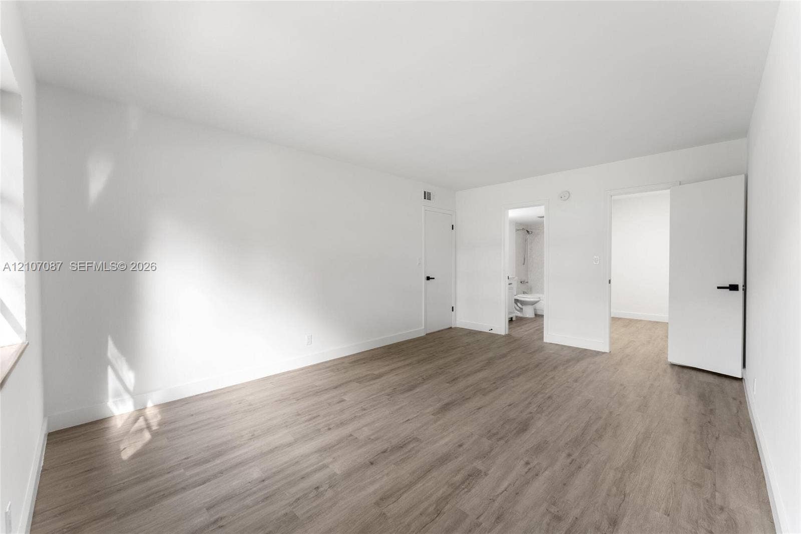 Interior space featuring wood-finish flooring, smooth white wall finishes, and matte black door hardware