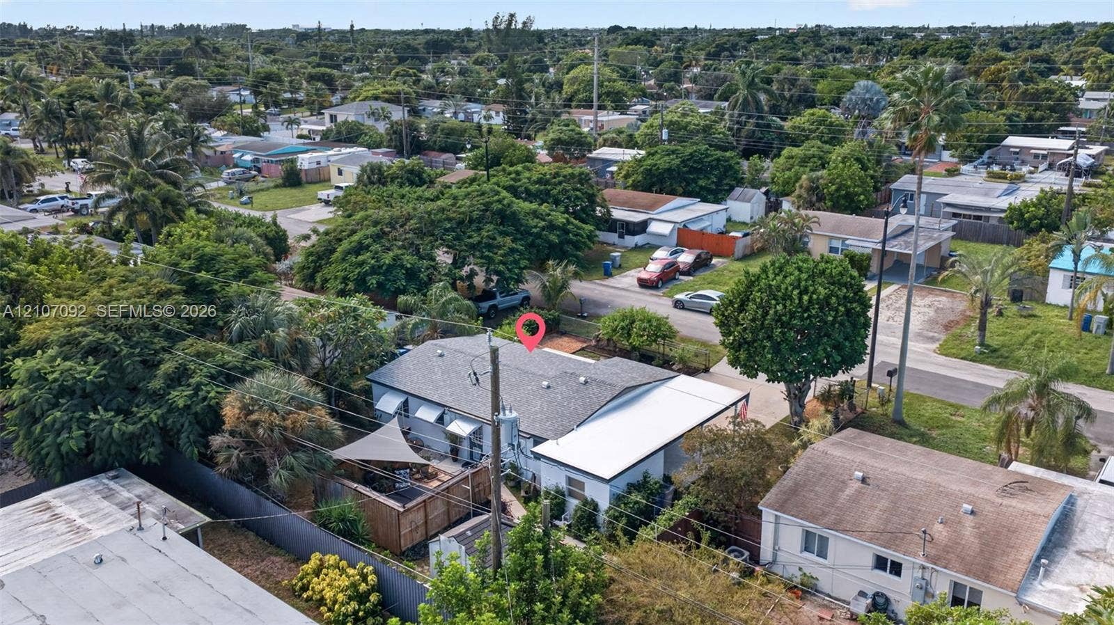 2864 NE 12th Terrace, Pompano Beach, FL 33064 Aerial perspective of a single-story residence featuring a shingled roof, an attached carport, and a fenced rear yard with mature trees and foliage