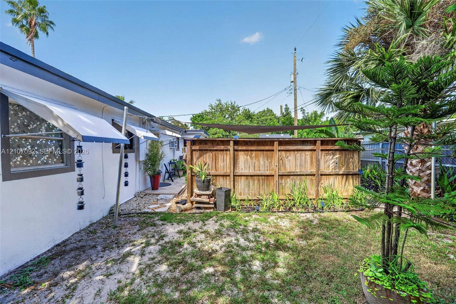 2864 NE 12th Terrace, Pompano Beach, FL 33064 Private outdoor space featuring a wood perimeter fence, retractable sun shade, wall-mounted window awnings, and established landscaping