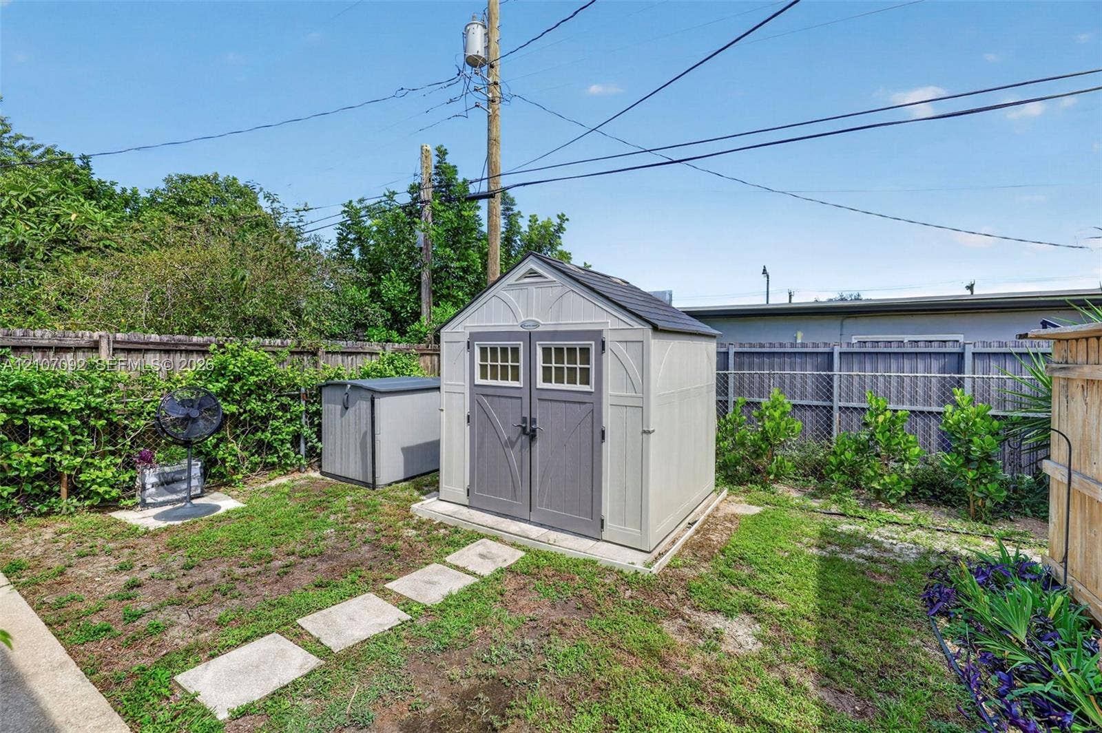2864 NE 12th Terrace, Pompano Beach, FL 33064 Exterior storage structure featuring a gable roof, double doors with glass paneling, and a reinforced foundation pad, situated within a fenced backyard
