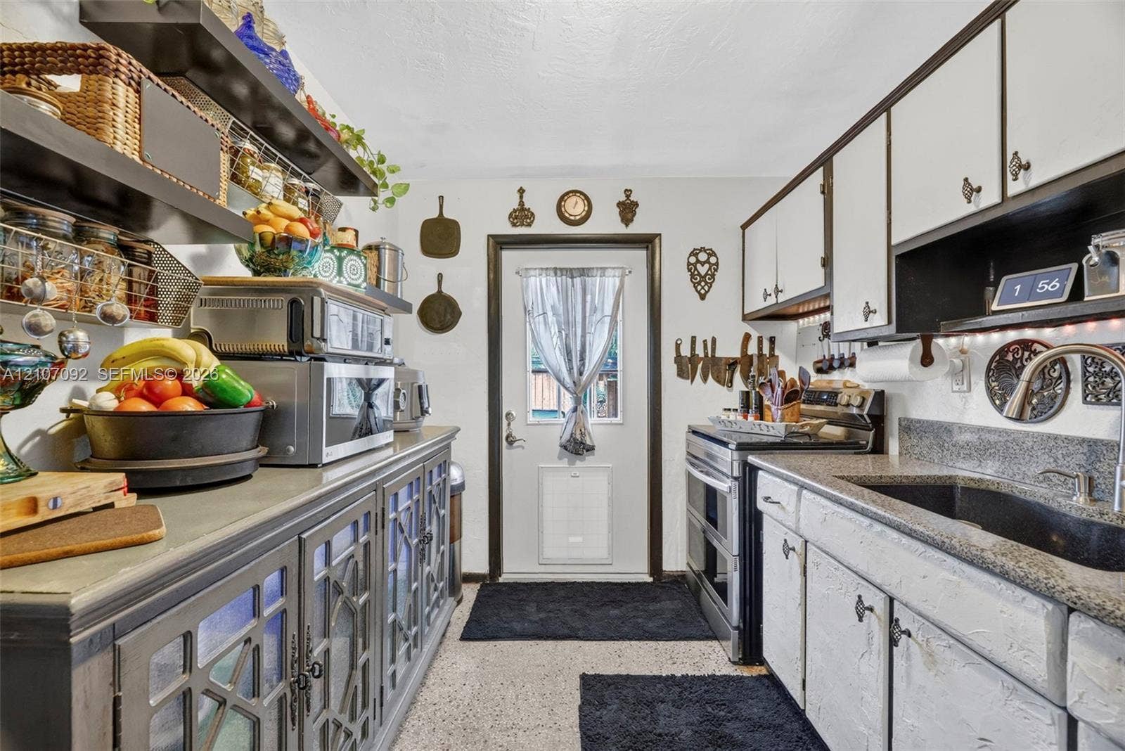 2864 NE 12th Terrace, Pompano Beach, FL 33064 Kitchen featuring two-tone cabinetry with glass-panel doors, dark stone-finish countertops, an undermount sink with a gooseneck faucet, open shelving, and a glass-paneled exterior door
