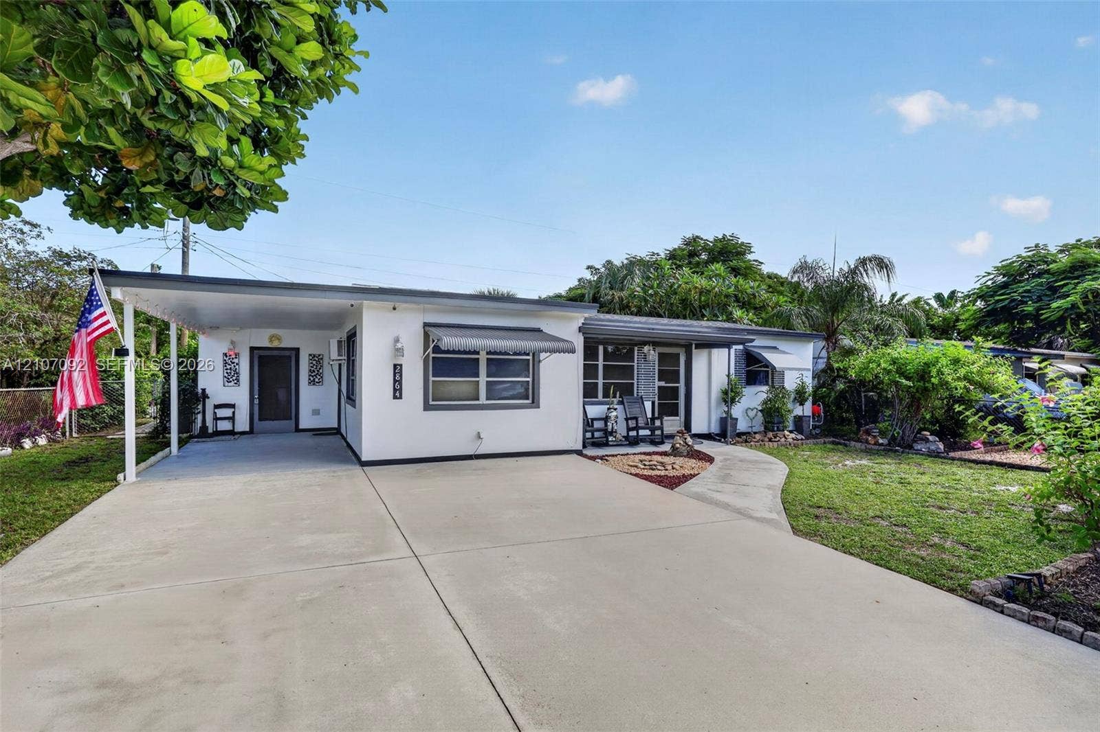 2864 NE 12th Terrace, Pompano Beach, FL 33064 Single-story exterior featuring a concrete driveway, attached carport, metal window awnings, and a covered front entryway