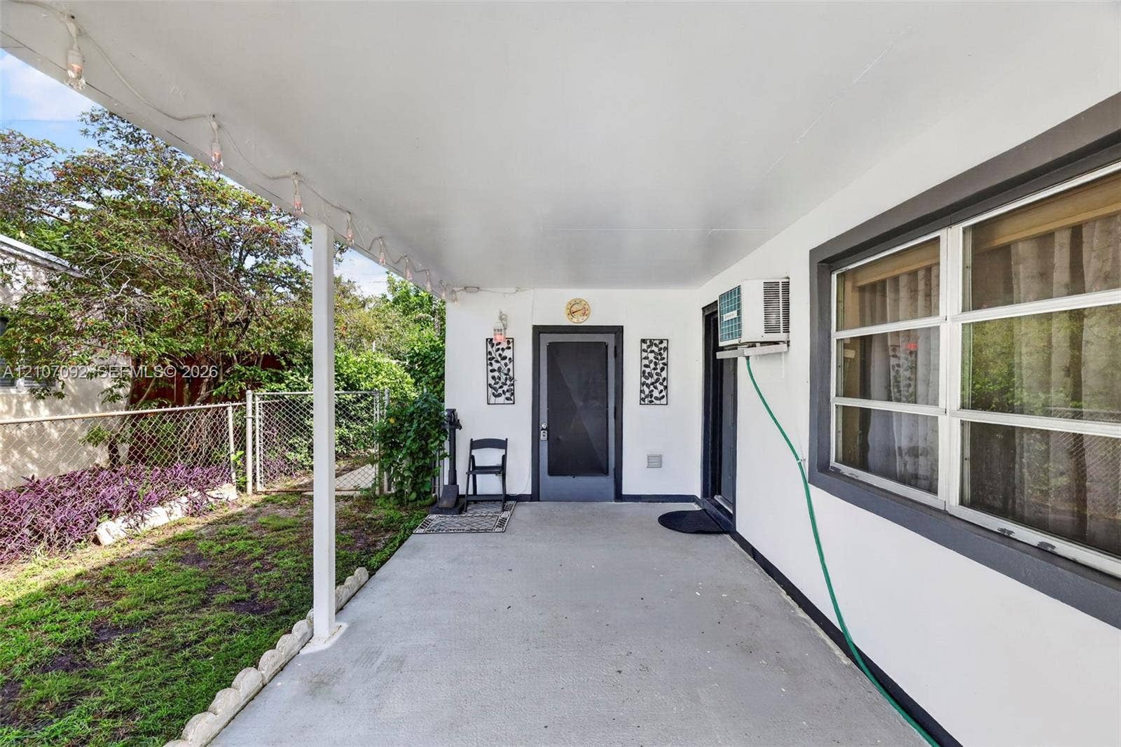 2864 NE 12th Terrace, Pompano Beach, FL 33064 Covered concrete patio featuring a clean white exterior finish, multi-pane windows with dark trim, and a secure entryway