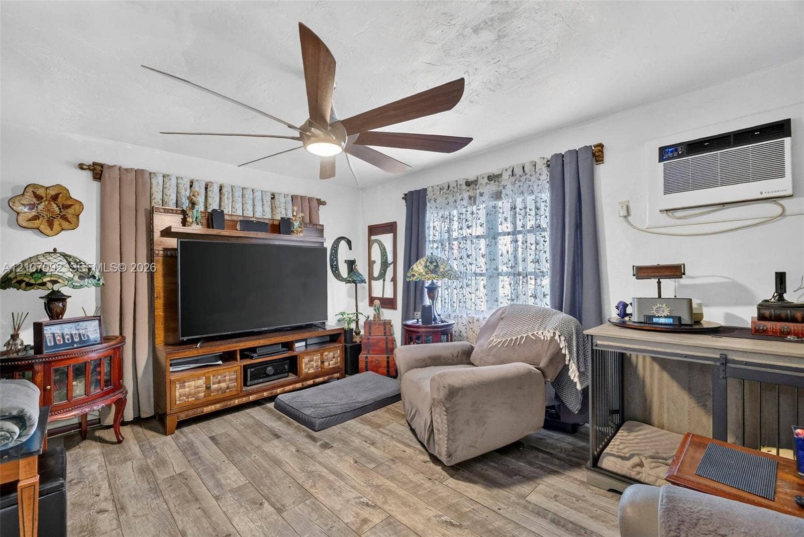 2864 NE 12th Terrace, Pompano Beach, FL 33064 Living area featuring wood-finish flooring, a multi-blade ceiling fan with integrated lighting, and a wall-mounted air conditioning unit
