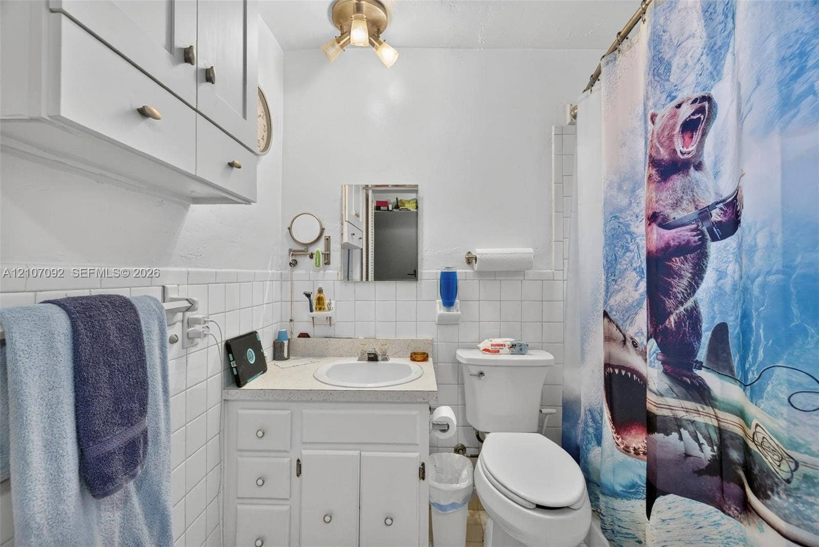 2864 NE 12th Terrace, Pompano Beach, FL 33064 Bathroom featuring white ceramic wall tile, a built-in vanity with integrated basin, upper wall-mounted cabinetry, and a three-light fixture