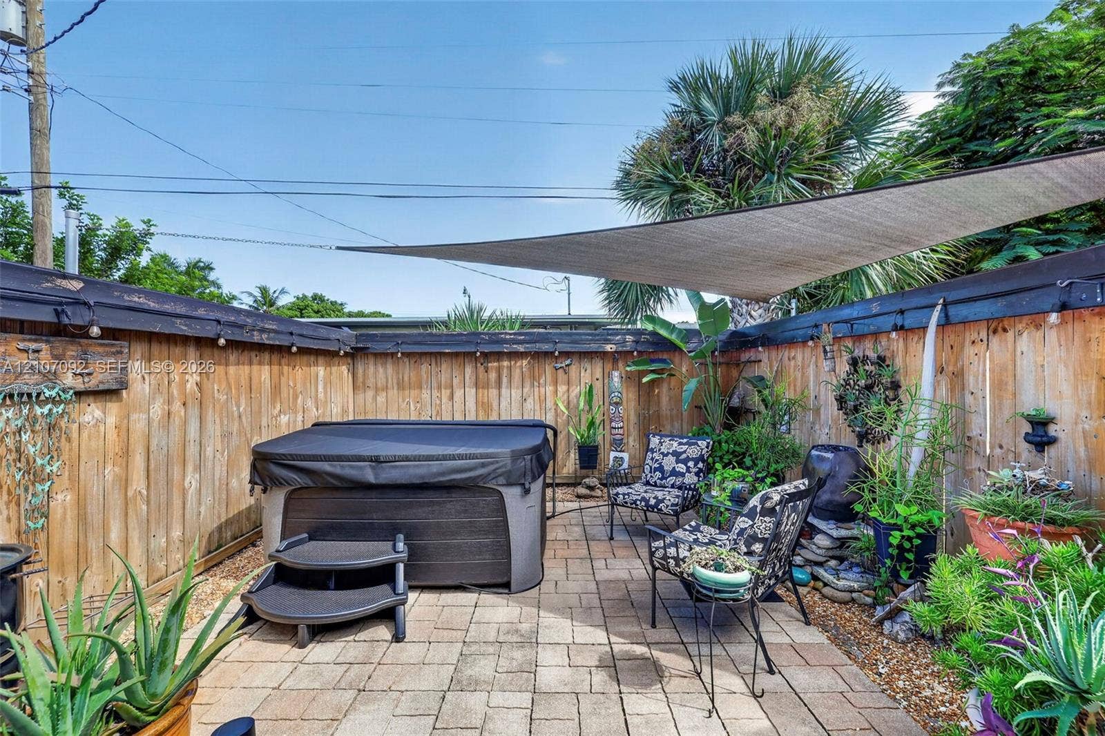 2864 NE 12th Terrace, Pompano Beach, FL 33064 Private outdoor space featuring a paved patio, high wood-plank fencing, built-in hot tub, and overhead shade sail