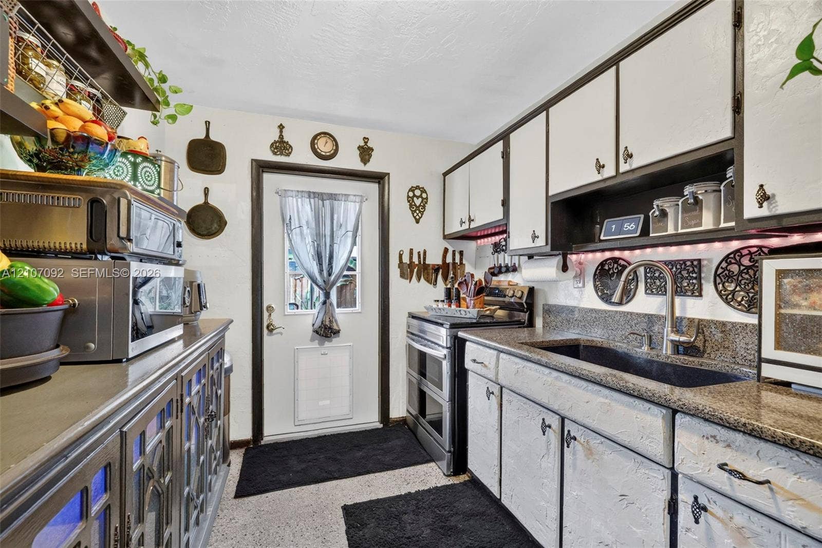 2864 NE 12th Terrace, Pompano Beach, FL 33064 Kitchen featuring stone-finish countertops, an undermount sink with a high-arch faucet, custom cabinetry with glass-panel detailing, and an exterior entry door