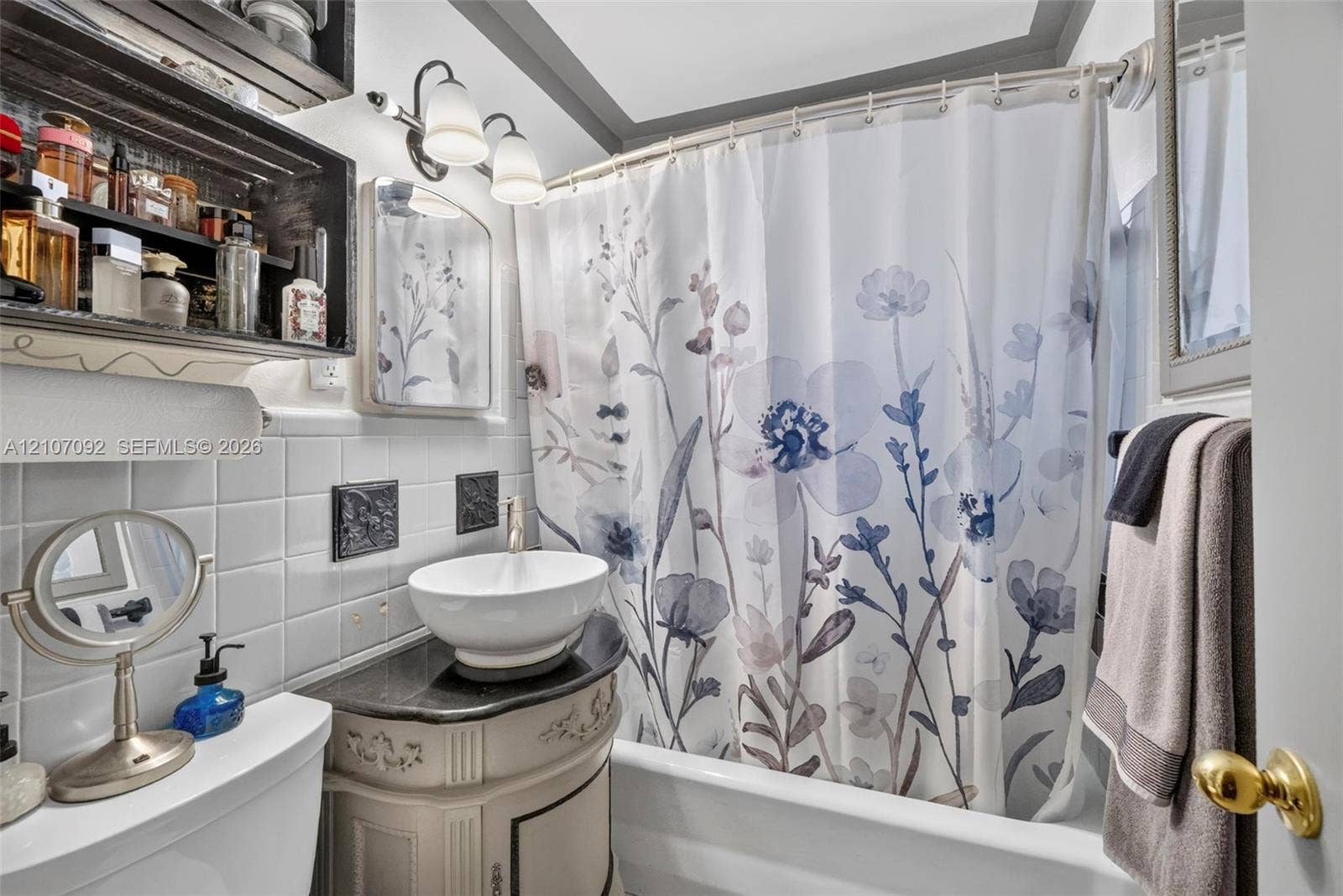 2864 NE 12th Terrace, Pompano Beach, FL 33064 Bathroom featuring a vessel sink with a dark stone-finish countertop, white square wall tile, built-in shelving, and dual-bulb vanity lighting