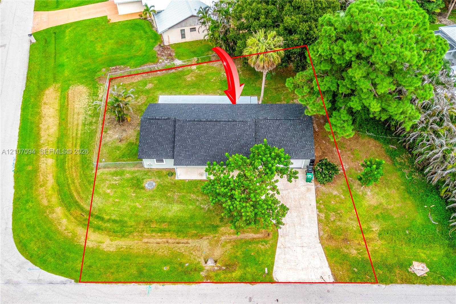 1131 SW London Lane, Port St Lucie, FL 34953 Aerial perspective of a property featuring a rectangular roofline, concrete driveway, fenced yard, and established landscaping including mature trees and palm specimens