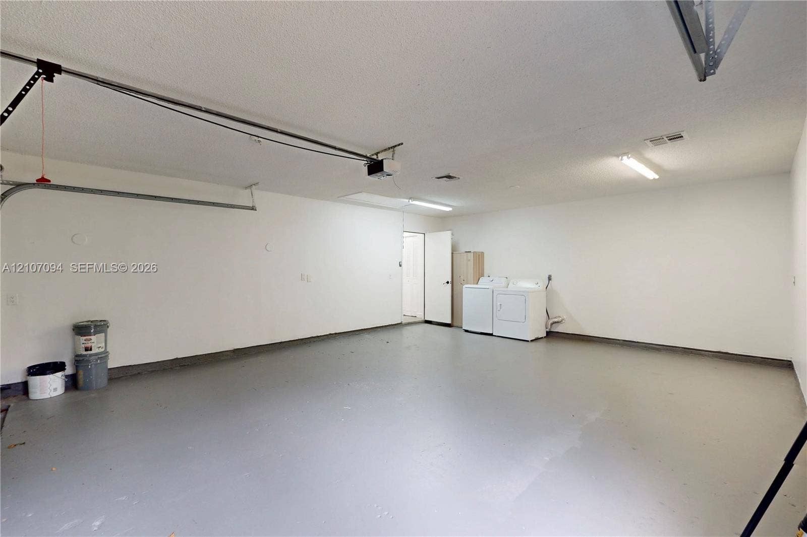 1131 SW London Lane, Port St Lucie, FL 34953 Two-car garage featuring a painted concrete floor, textured ceiling, fluorescent lighting, and dedicated laundry hookups