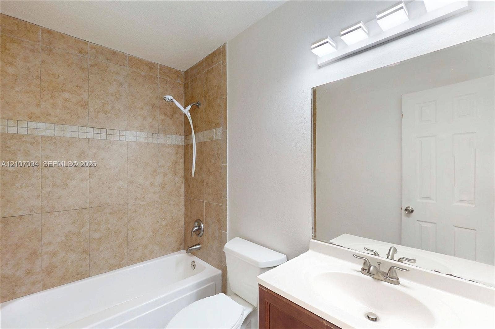 1131 SW London Lane, Port St Lucie, FL 34953 Bathroom featuring a tiled tub surround with decorative accent inlay, a vanity with an integrated basin, a large wall-mounted mirror, and a four-light fixture