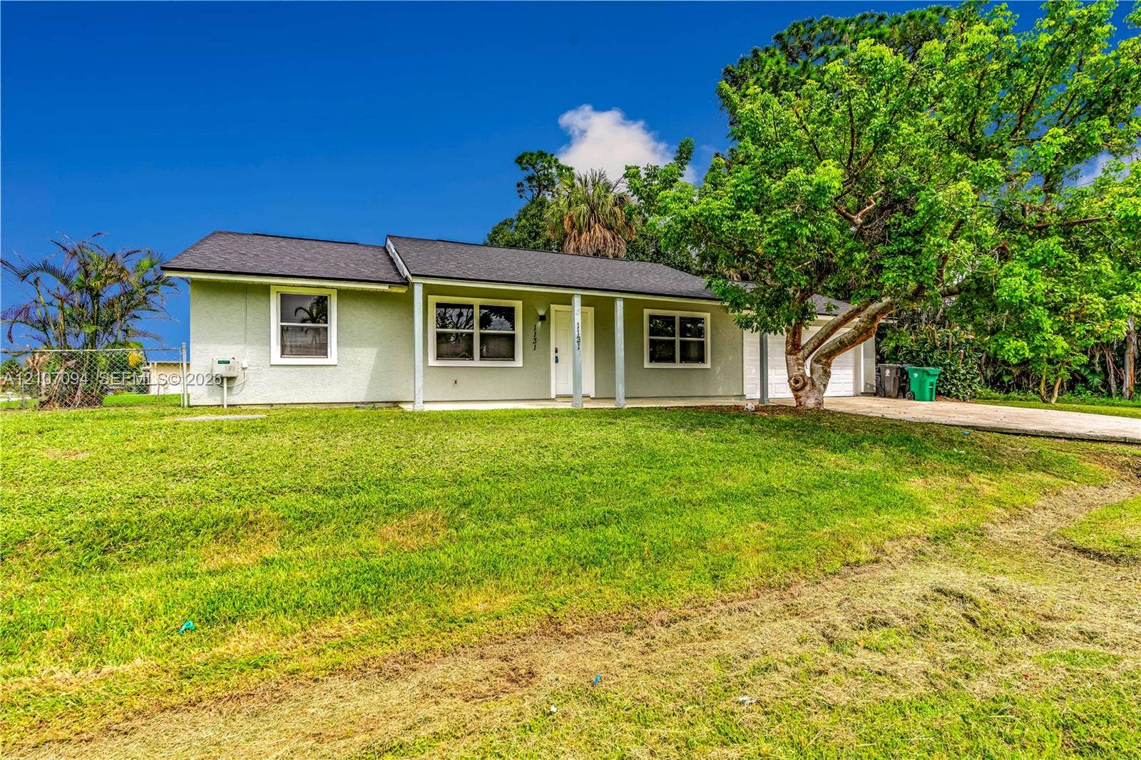 1131 SW London Lane, Port St Lucie, FL 34953 Single-story exterior featuring a light-colored facade, dark shingled roof, covered front entryway, and an attached garage