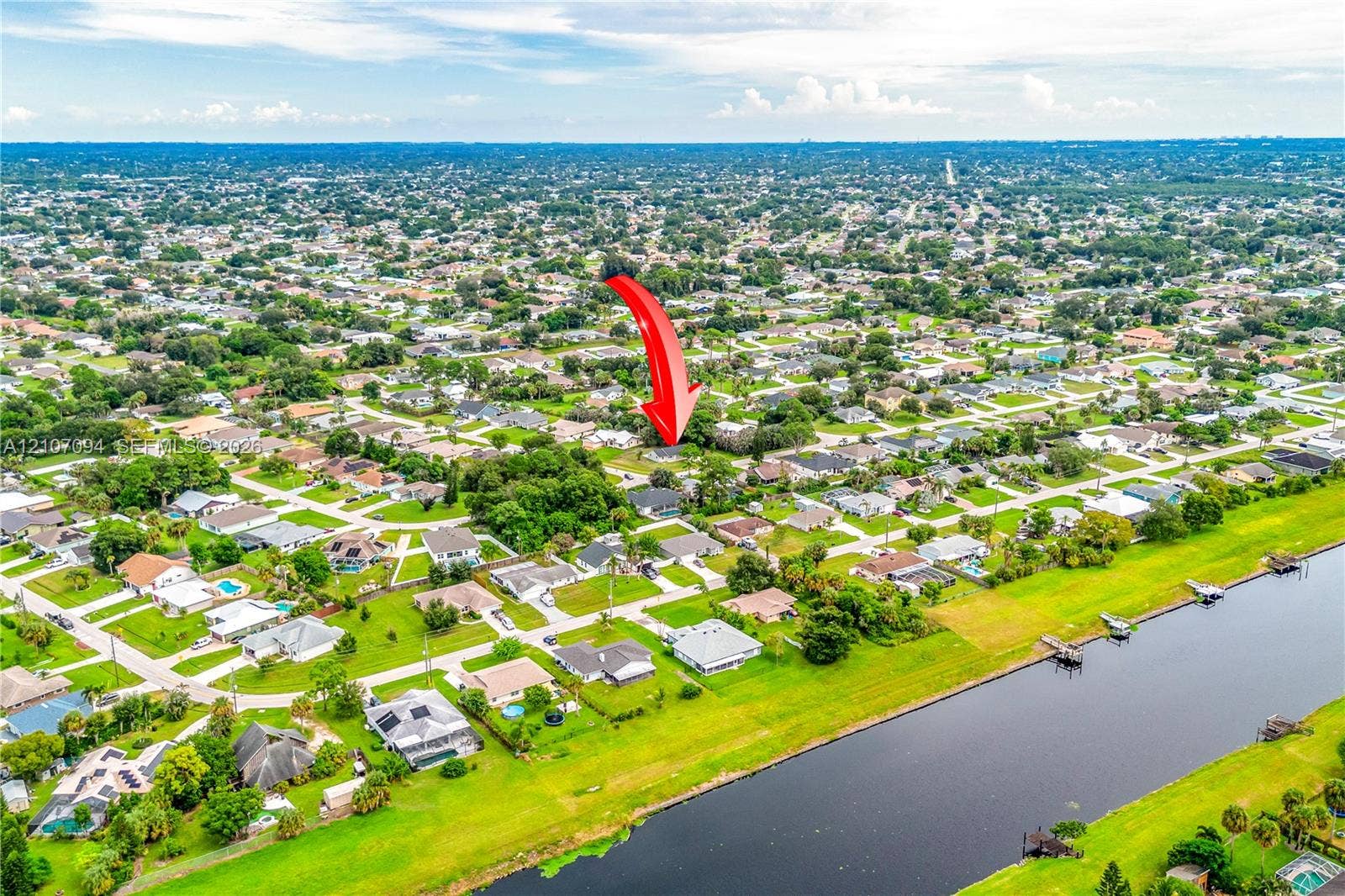 1131 SW London Lane, Port St Lucie, FL 34953 Aerial view of the residential property featuring mature trees, a multi-pitched roofline, and access to a canal