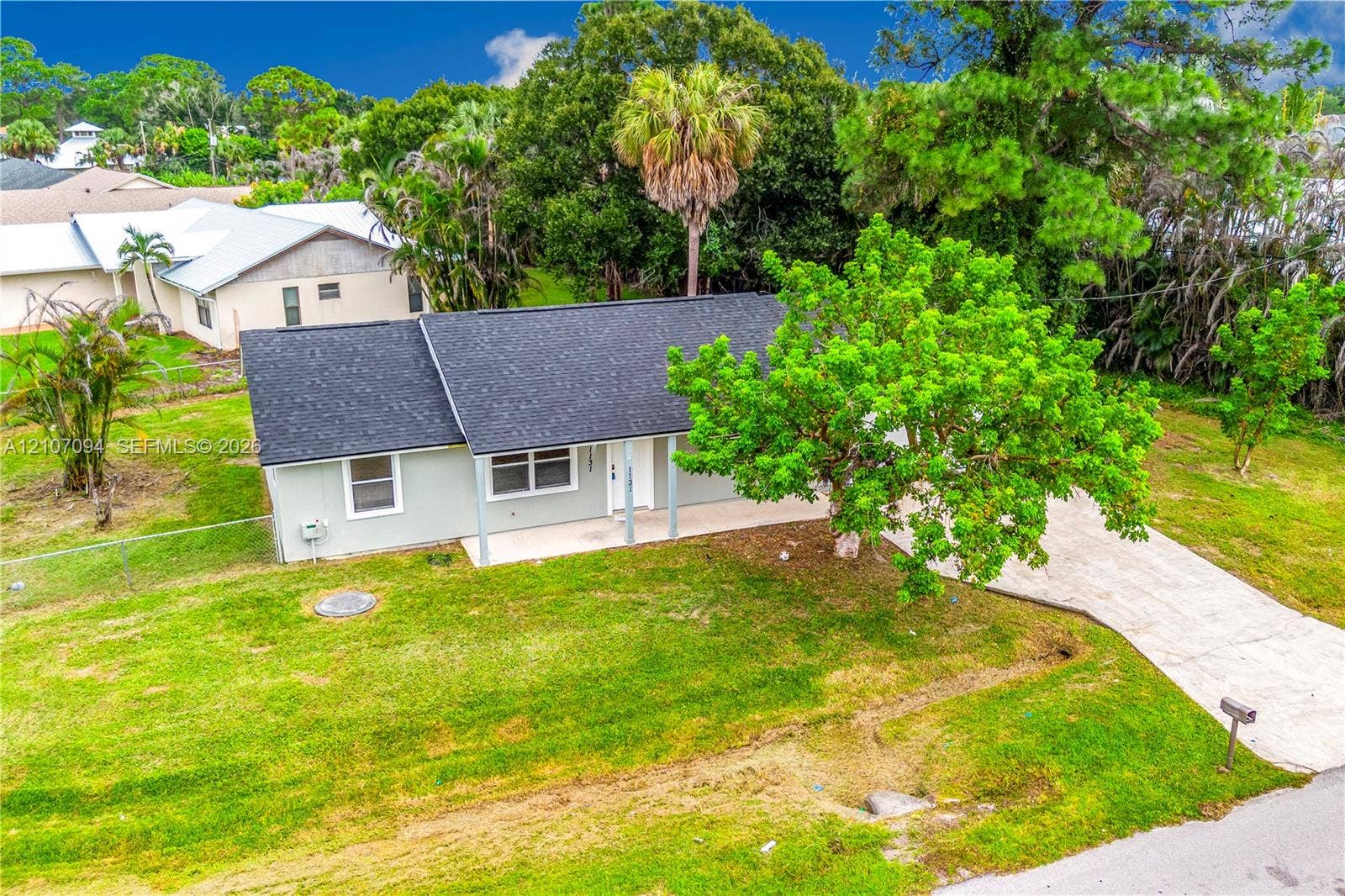 1131 SW London Lane, Port St Lucie, FL 34953 Single-story exterior featuring a shingled roof, light-toned siding, concrete driveway, and covered front entry
