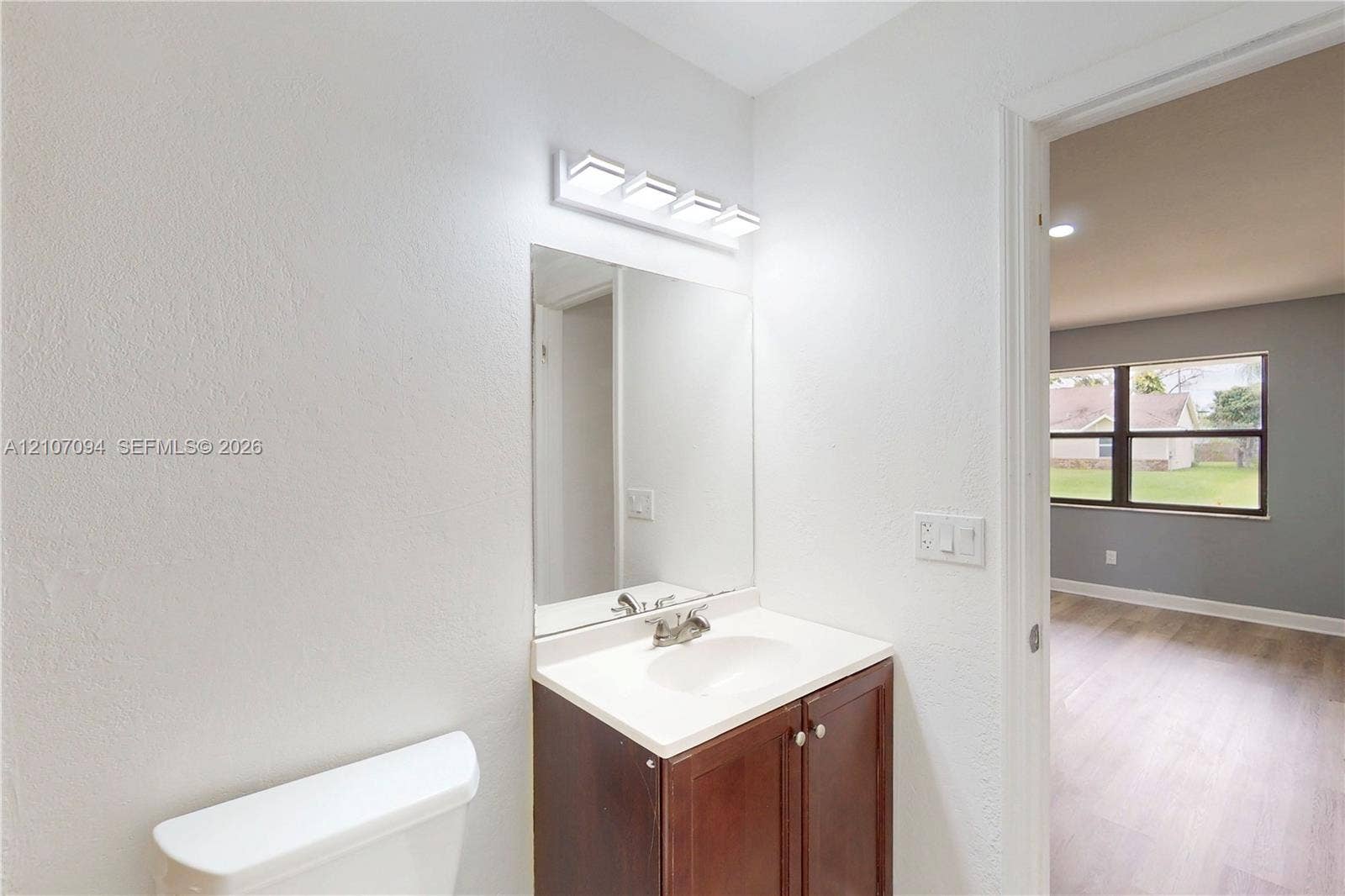 1131 SW London Lane, Port St Lucie, FL 34953 Bathroom featuring a dark wood-finish vanity with a white countertop, integrated basin, four-light vanity fixture, and frameless mirror