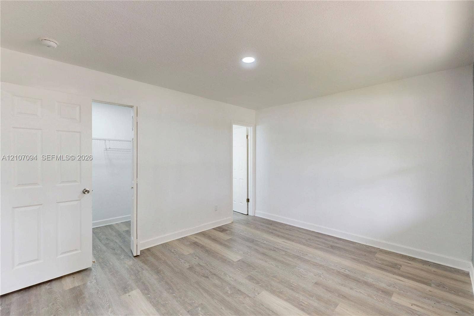 1131 SW London Lane, Port St Lucie, FL 34953 Room featuring wood-finish flooring, recessed lighting, and a six-panel door leading to a walk-in closet with built-in shelving