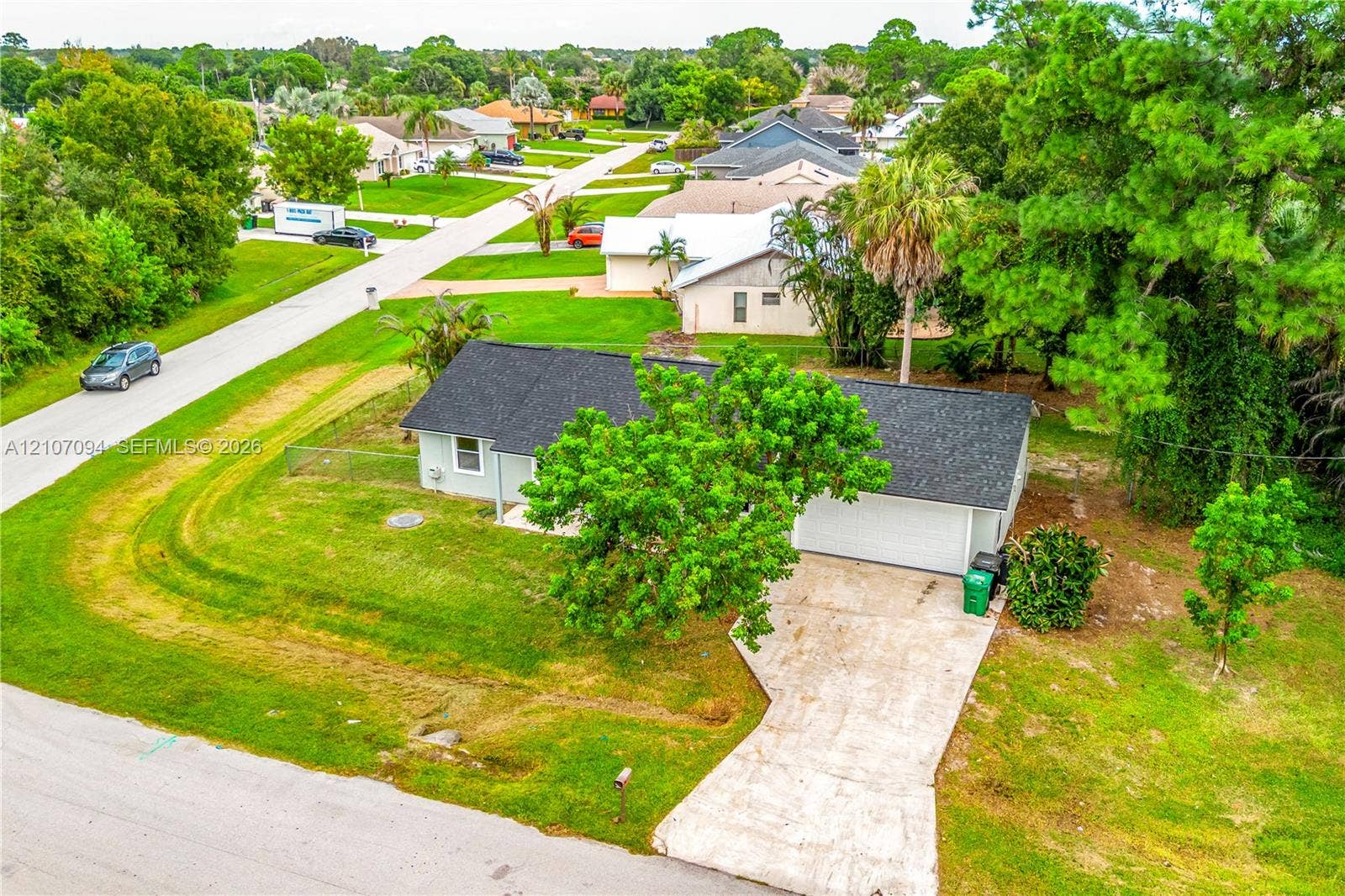 1131 SW London Lane, Port St Lucie, FL 34953 Single-story residence featuring a shingled roof, attached two-car garage, concrete driveway, and established landscaping on a corner lot