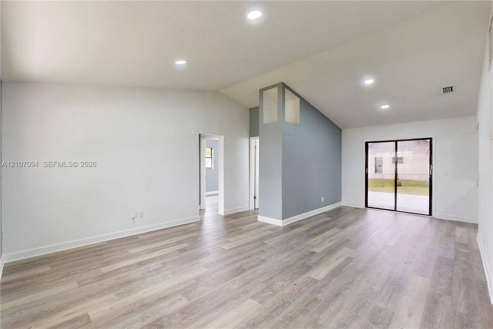 1131 SW London Lane, Port St Lucie, FL 34953 Vaulted ceilings, wood-finish flooring, recessed lighting, accent wall, and sliding glass doors