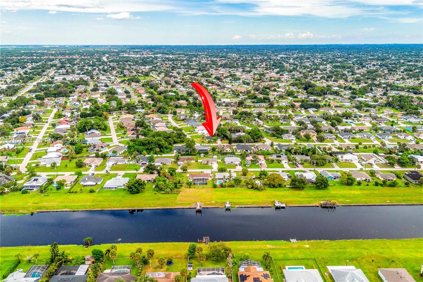 1131 SW London Lane, Port St Lucie, FL 34953 Aerial perspective featuring a residential lot with water frontage along a canal and mature landscaping